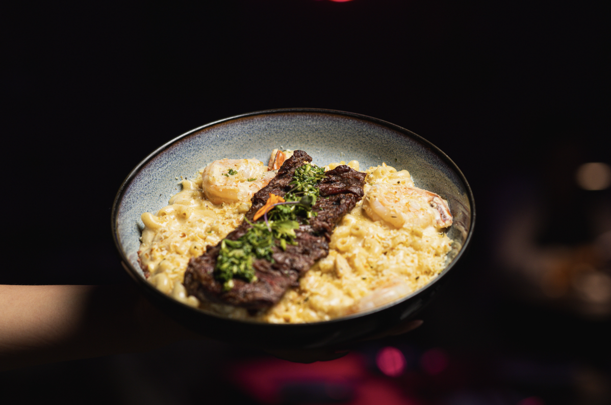A bowl of shrimp and creamy pasta topped with grilled steak and garnished with herbs.