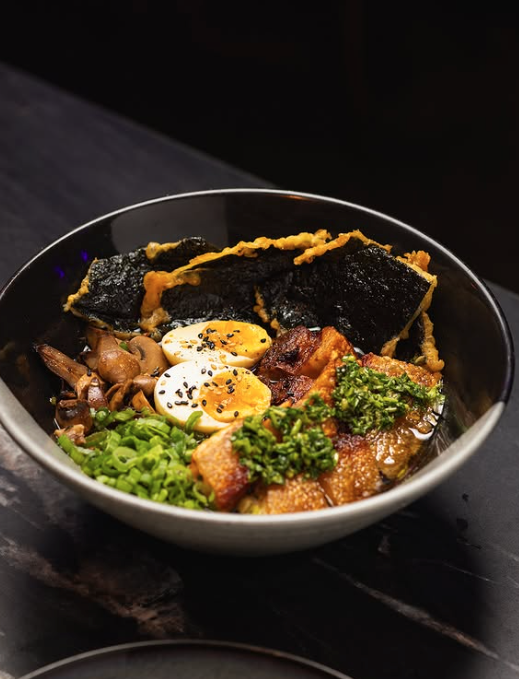 A bowl of ramen with sliced pork, boiled eggs, seaweed, green onions, and mushrooms.