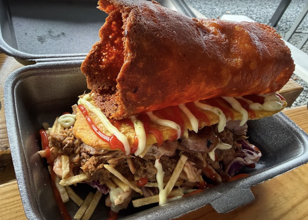 A large po’ boy sandwich with fried fish, shredded lettuce, tomato, mayonnaise, and ketchup in a toasted sub roll.