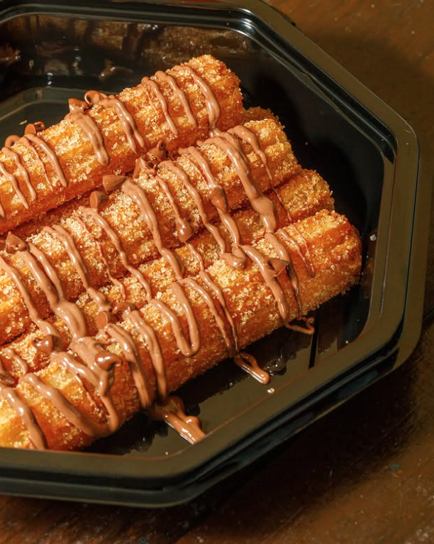 Fried banana spring rolls drizzled with chocolate sauce in a black container.