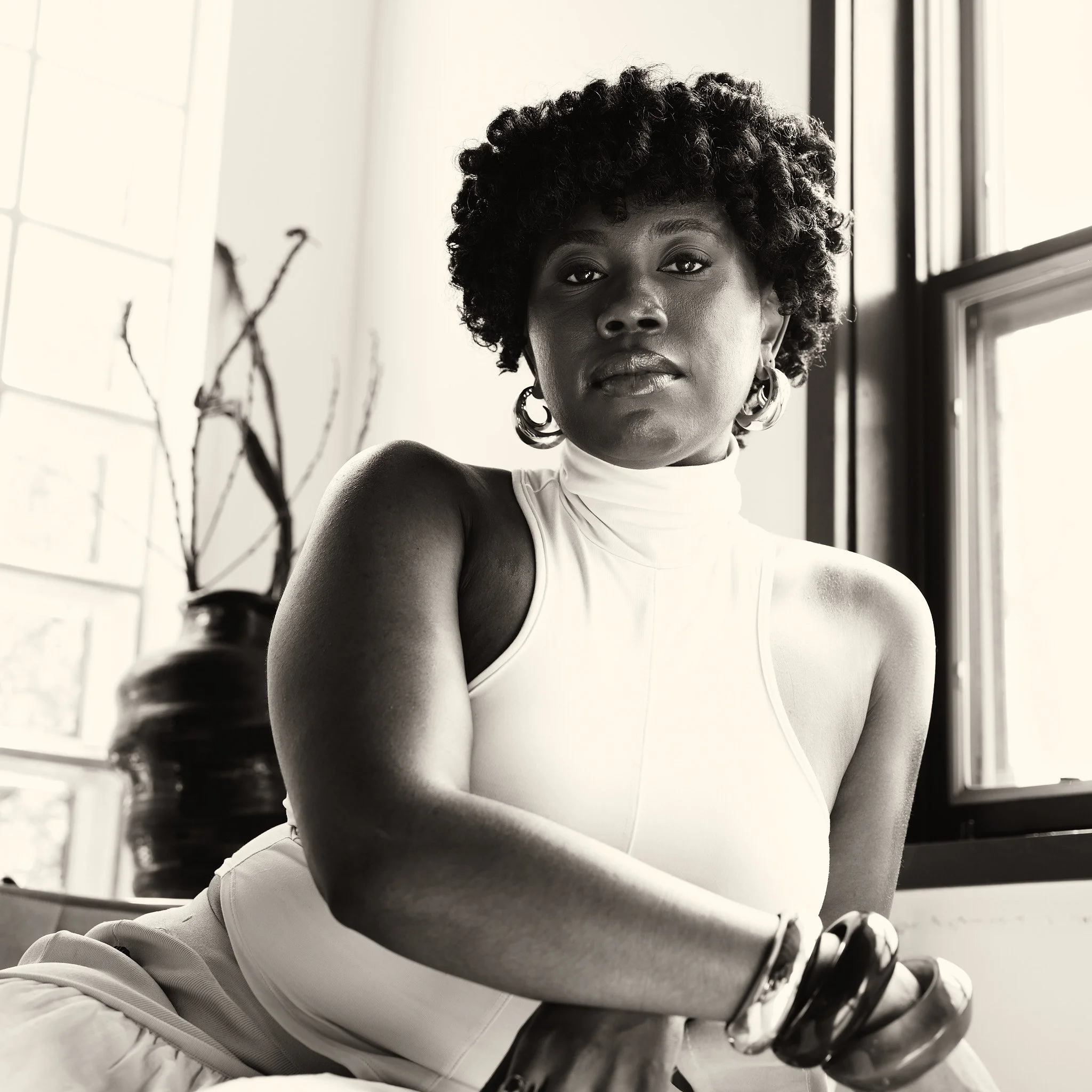 Ekep Nkwelle seated beside a window in a white outfit