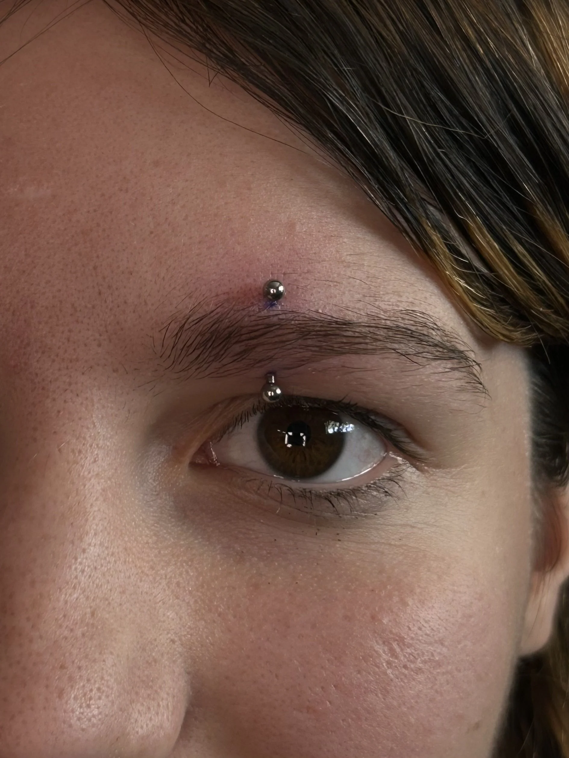 Close-up image of a person's face focusing on the eye with a dermal piercing above the eyebrow.