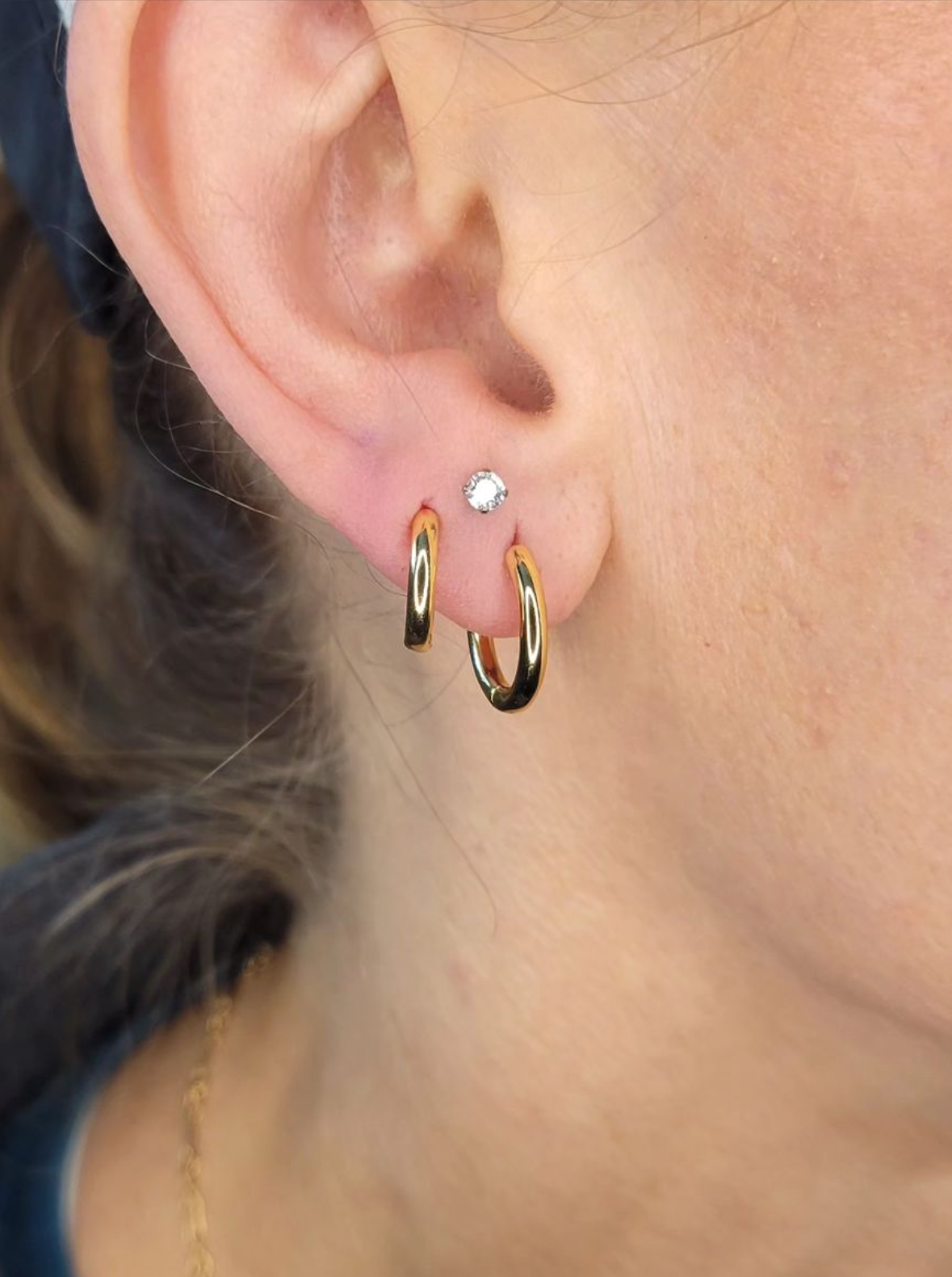 Close-up of a woman's ear with multiple earrings: a small diamond stud, a gold hoop, and a larger gold hoop earring.