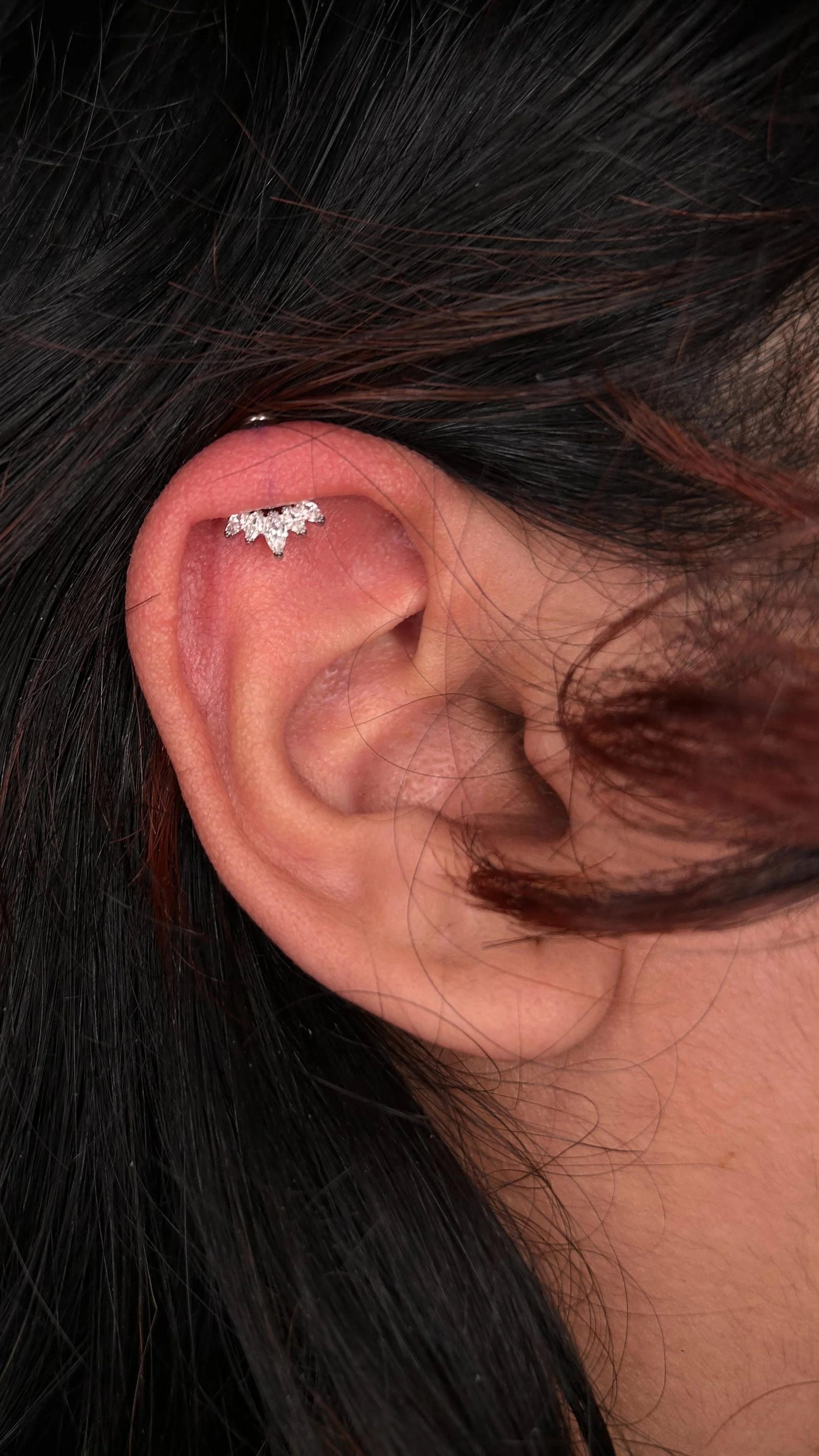 Close-up of a human ear with a decorative silver earring with small gemstones.