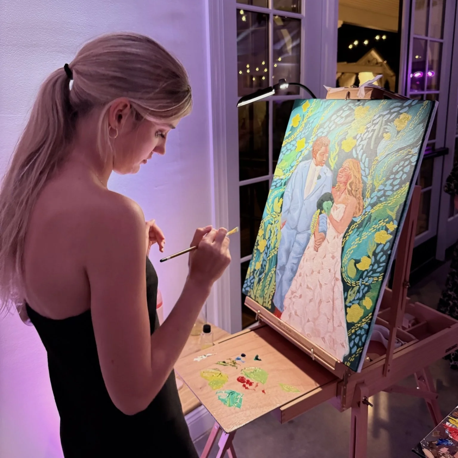 A woman painting a large canvas of a romantic scene, with a man and woman in formal attire, surrounded by colorful, lush foliage, in a well-lit indoor space.