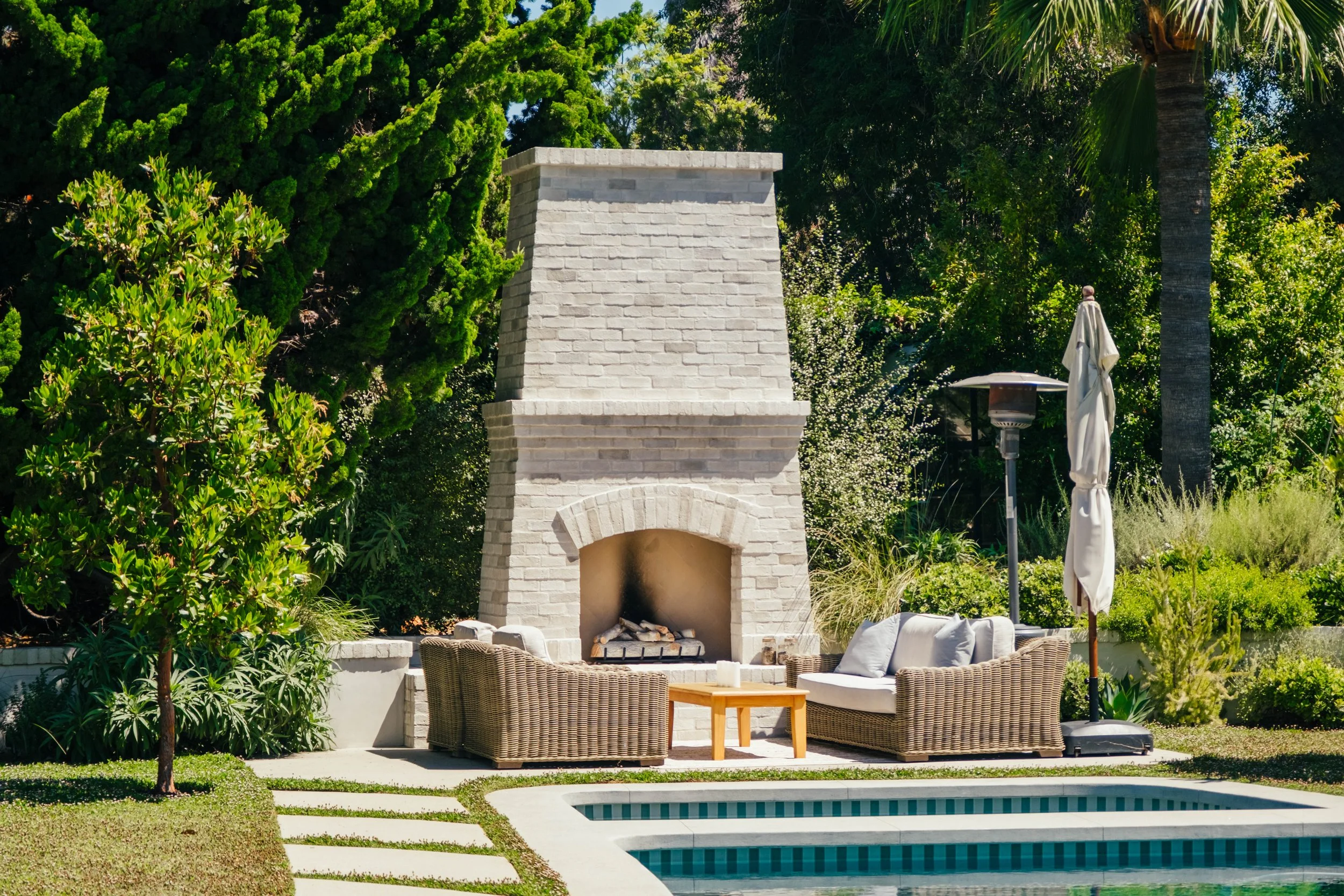 Outdoor fireplace and pool surrounded by residential landscaping by Rosewood Landscape