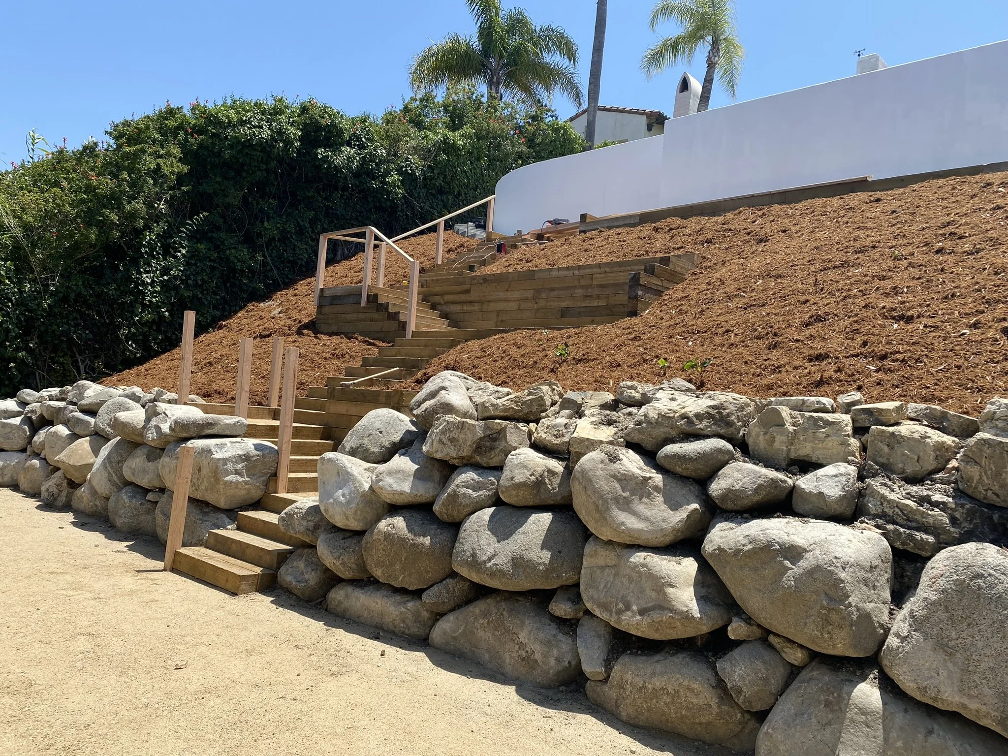 Hillside stairs with natural boulder retaining wall and terraced landscaping by Rosewood Landscape