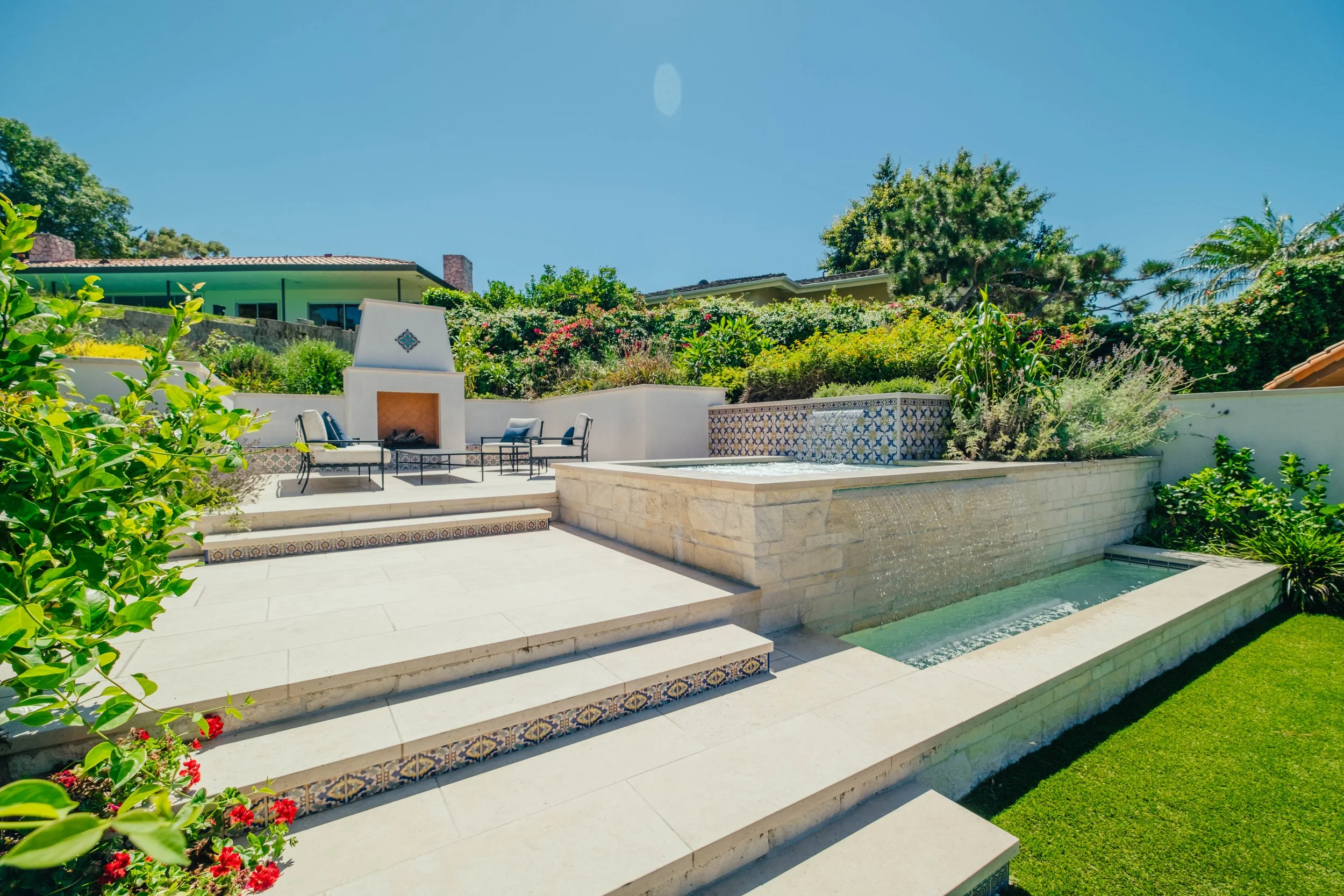 Raised spa with cascading water feature, tiled steps and outdoor fireplace by Rosewood Landscape