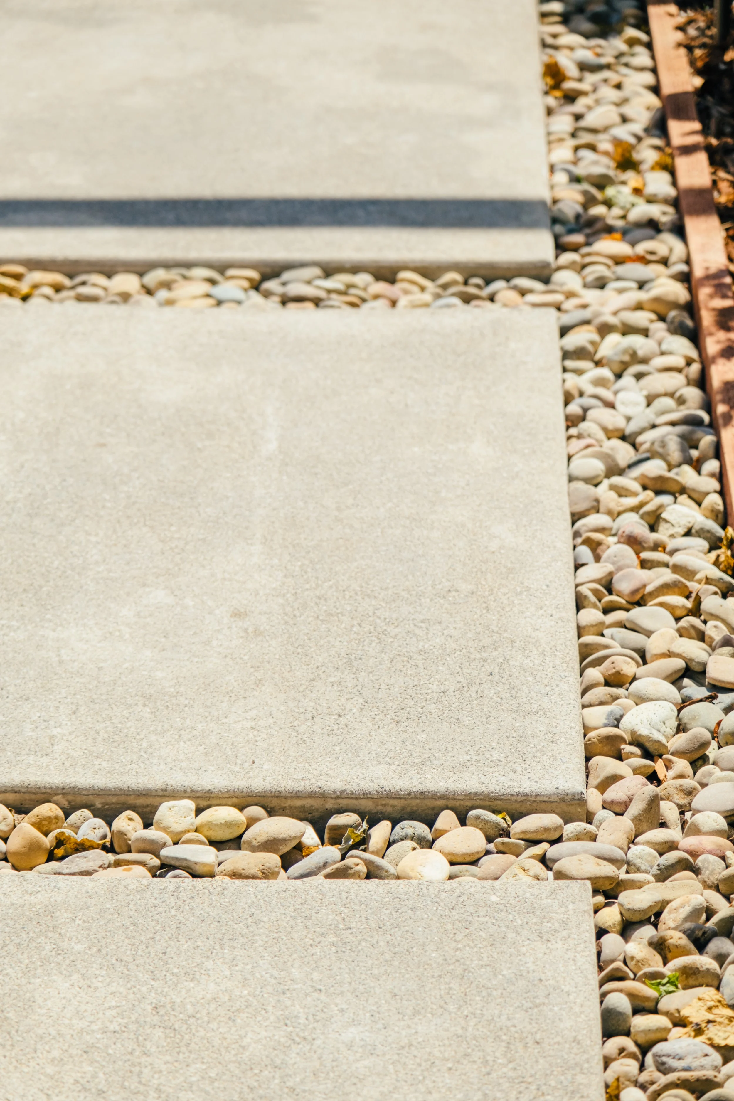 Modern concrete stepping stones with decorative river rock landscaping by Rosewood Landscape