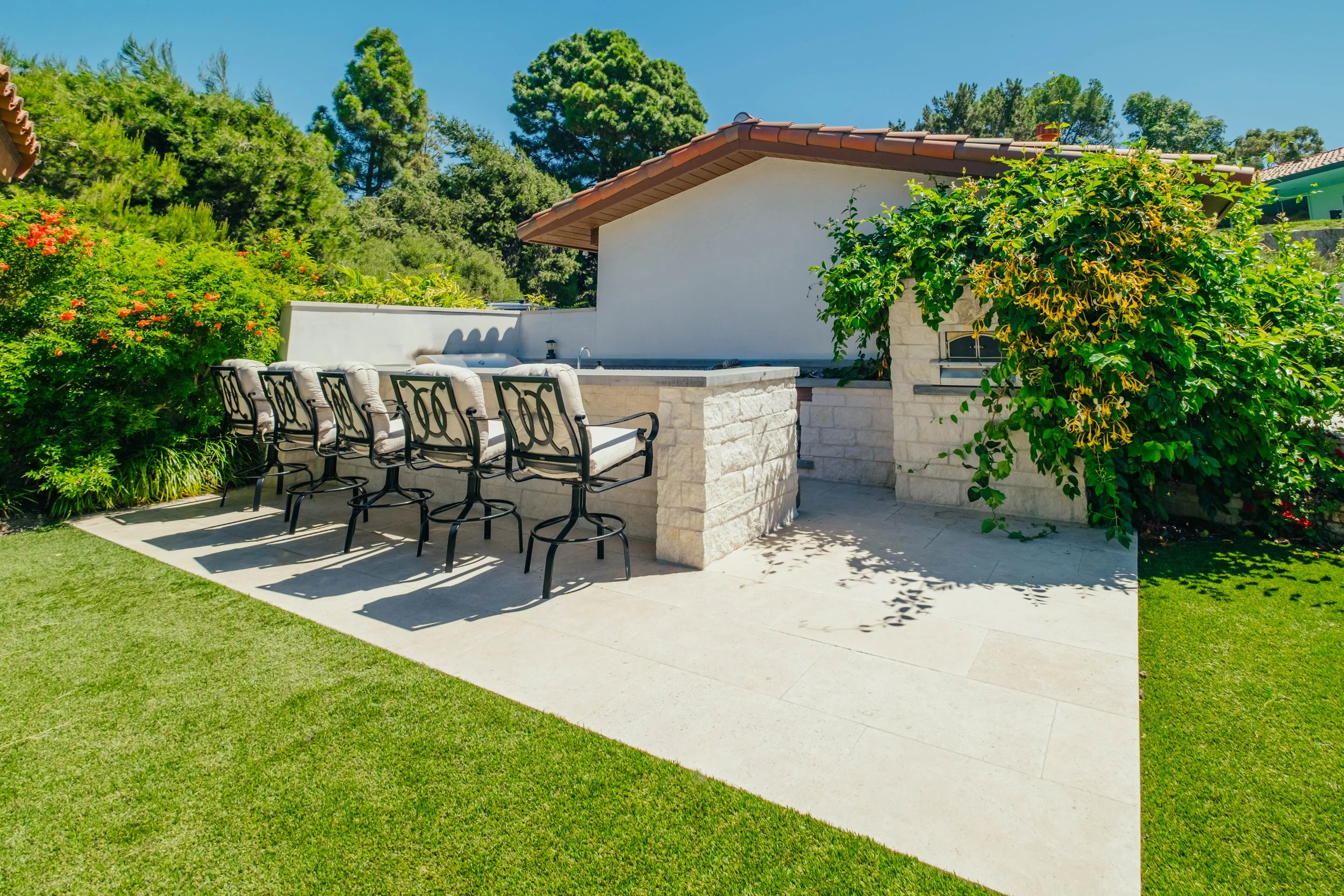 Custom outdoor kitchen with stone bar seating, patio and surrounding landscaping by Rosewood Landscape