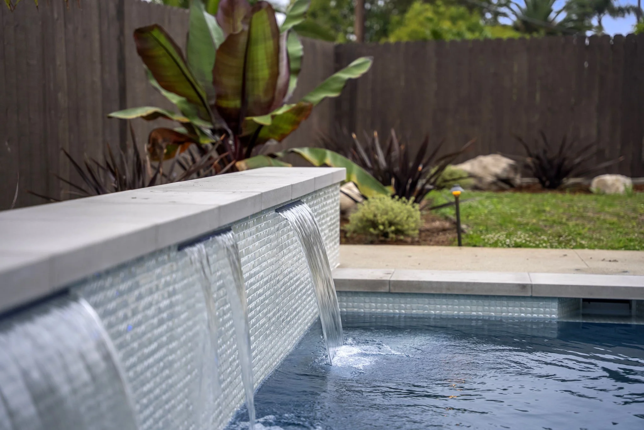 Custom pool and spa with tiled waterfall feature and surrounding landscaping by Rosewood Landscape