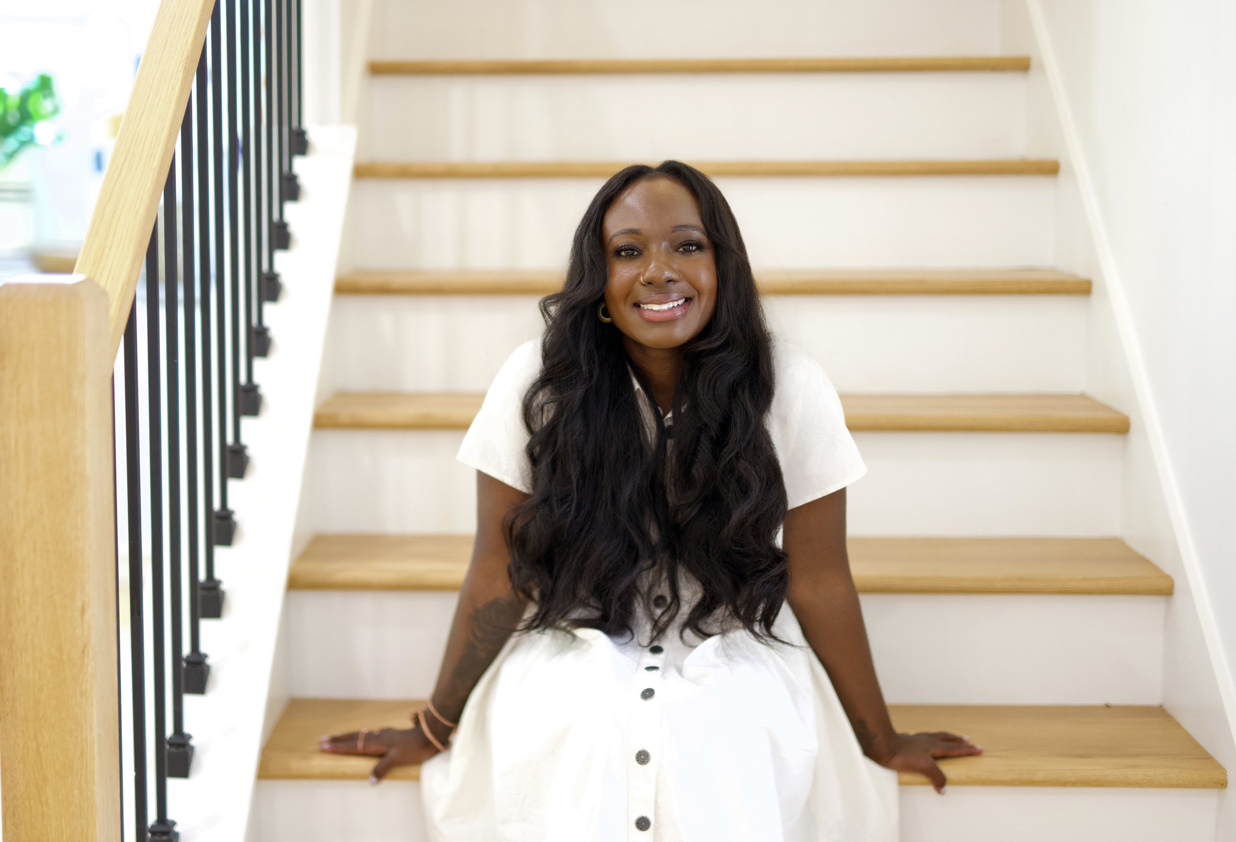 Shay Wilson, Atlanta real estate agent, smiling on a staircase in a white dress