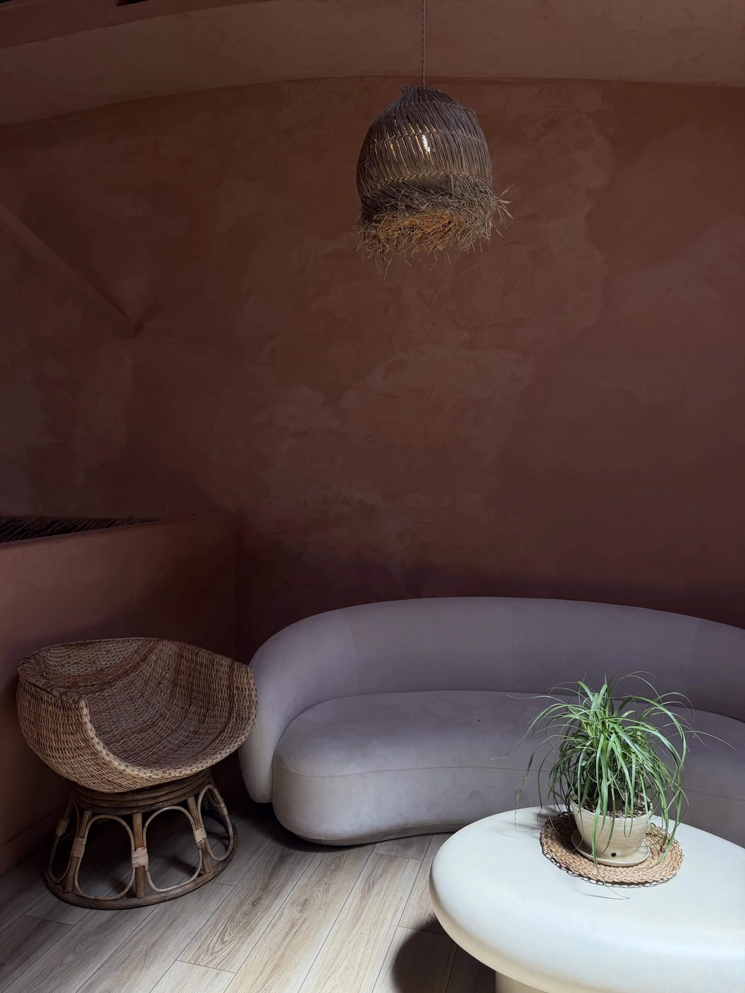 living room with a curved white sofa, rattan accent chair and a round side table with a potted plant