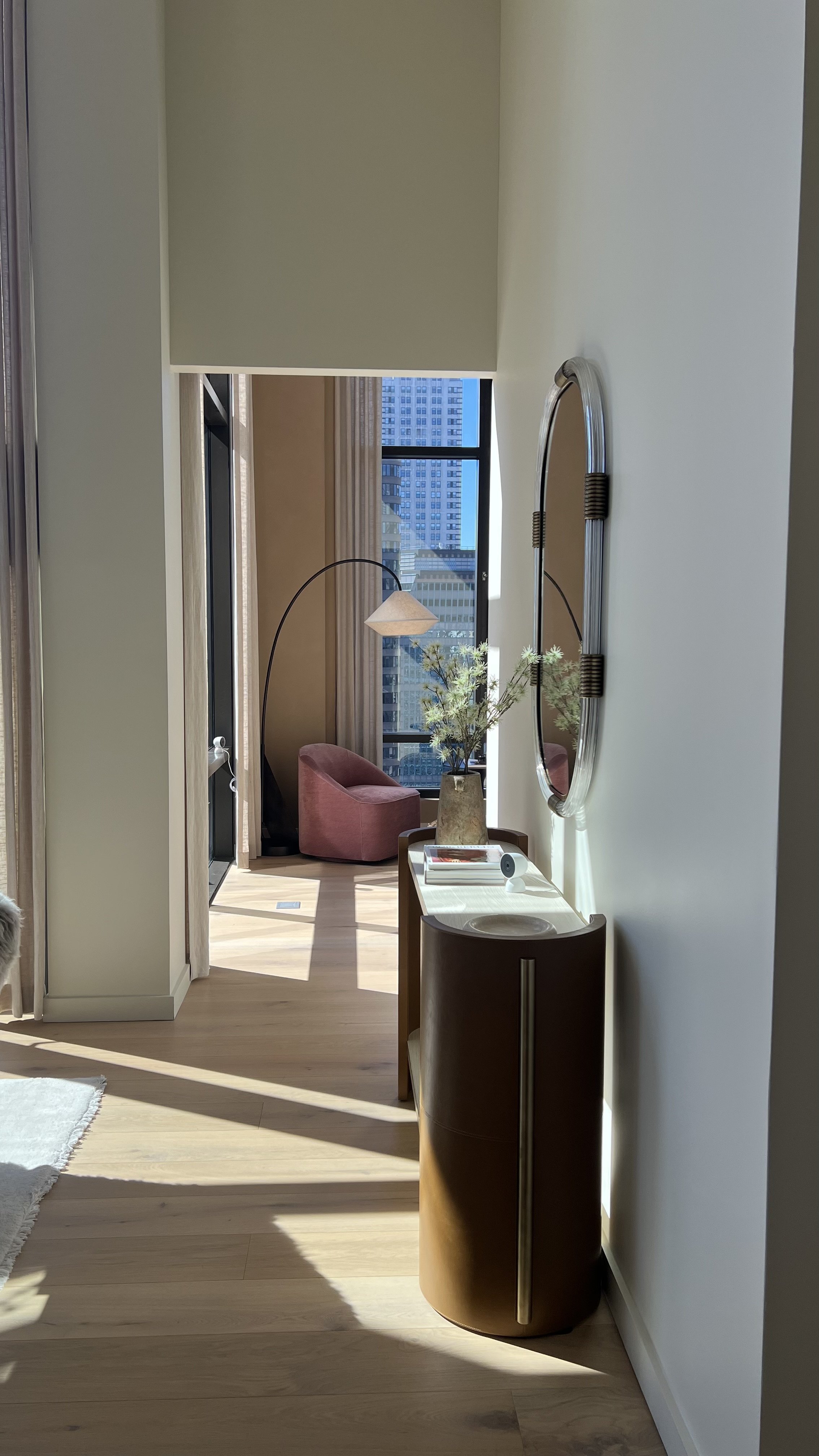 sunlit apartment hallway with a round mirror and console table, city views through the window