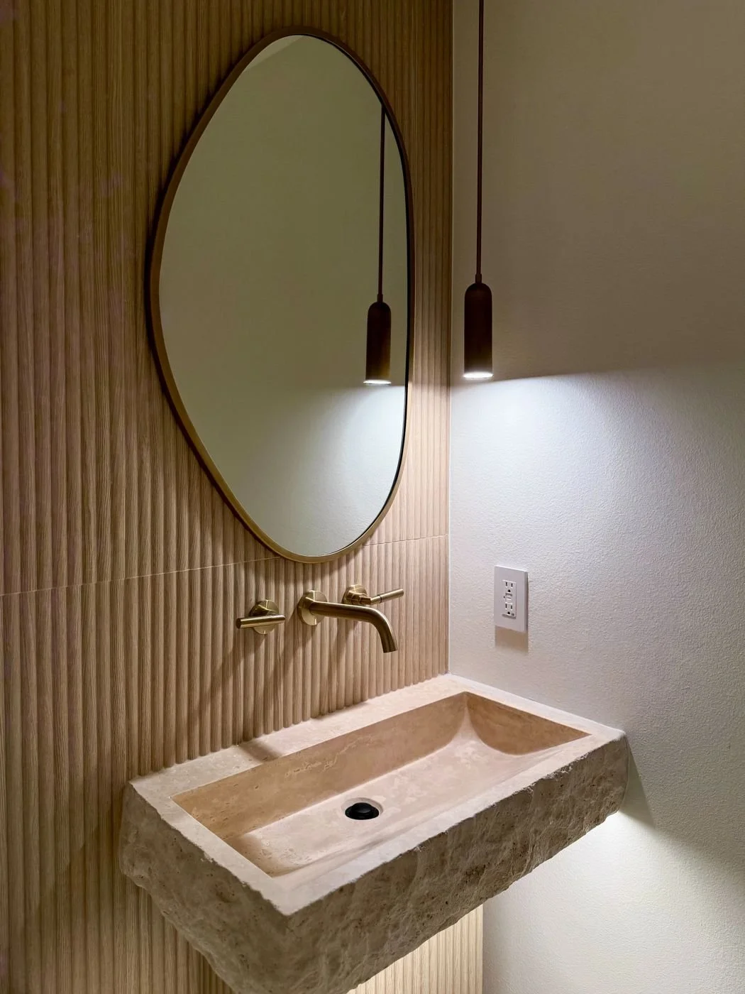powder room with a stone vessel sink, fluted wood wall and brass fixtures