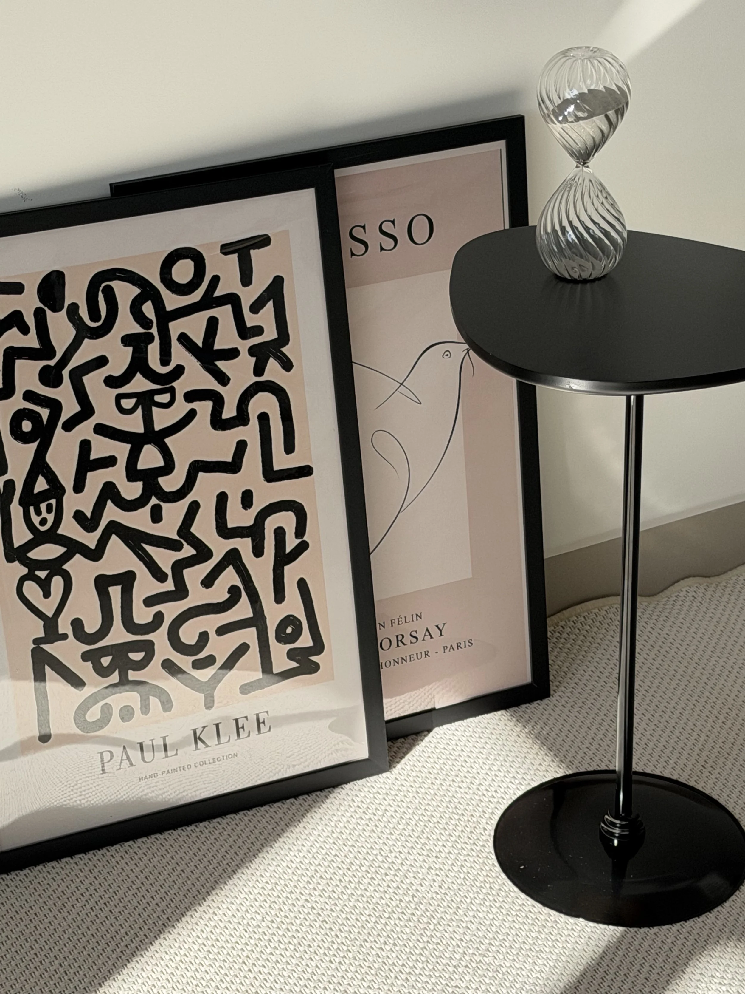 framed black and white line-art prints leaning against a wall beside a black side table