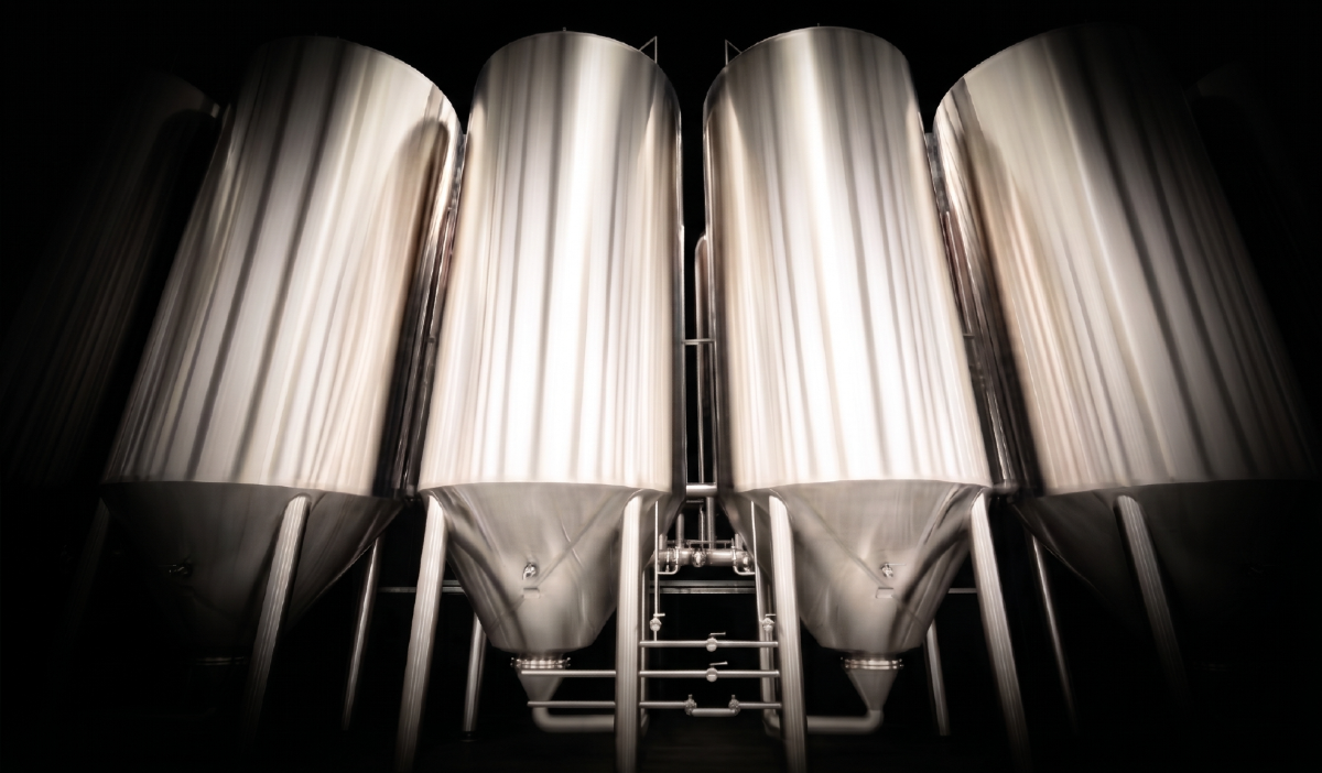 Four large stainless steel fermentation tanks in a brewery or winery facility.