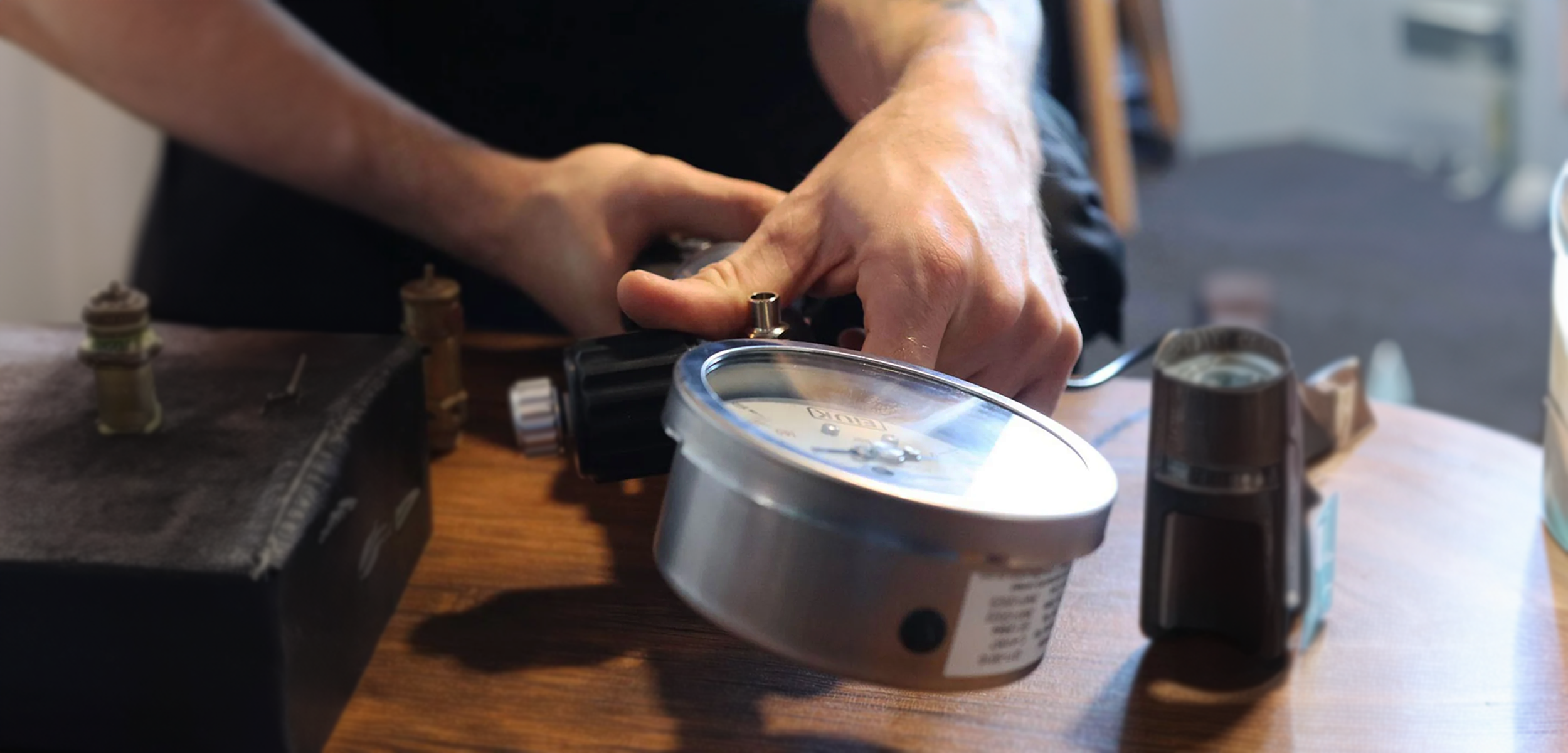Person's hand adjusting a device on a wooden surface with various tools and a tape measure nearby.