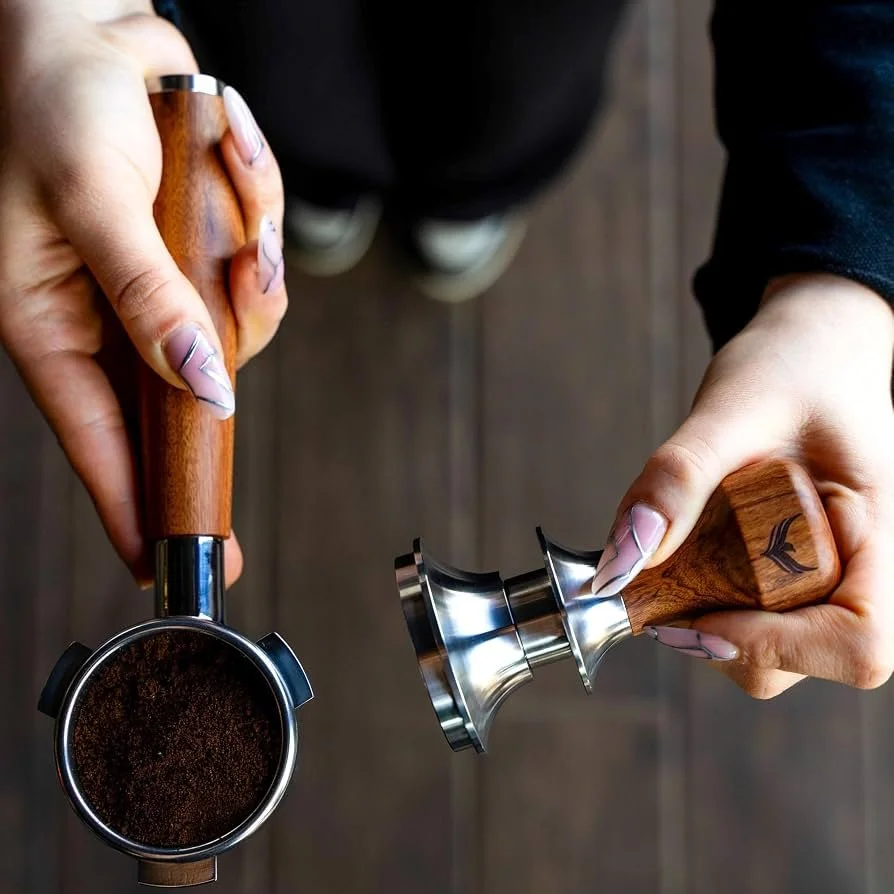 Two hands holding a coffee tamp and a coffee distributor, preparing to make espresso.