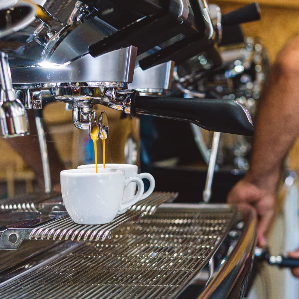 Close-up of espresso machine pouring coffee into a white ceramic cup on a metal drip tray.