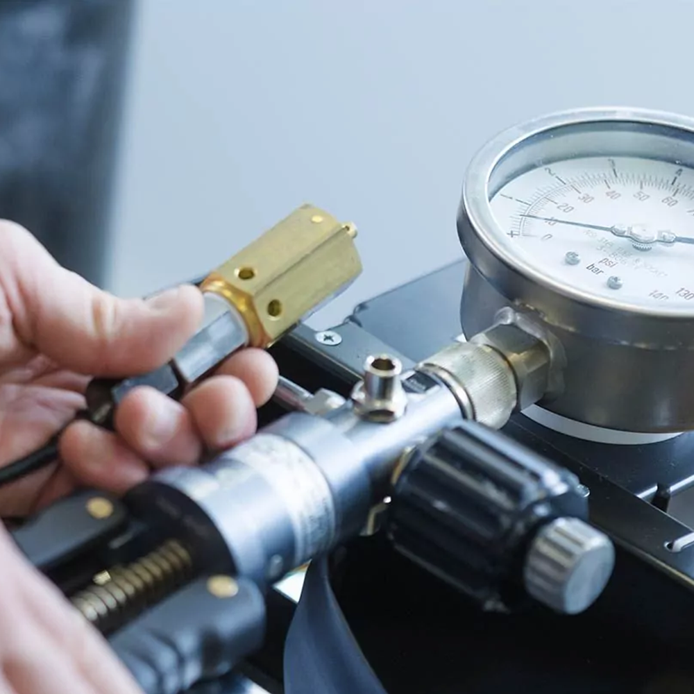 A person adjusting a pressure gauge on a metal laboratory or industrial instrument with a dial displaying measurements in psi and bar.