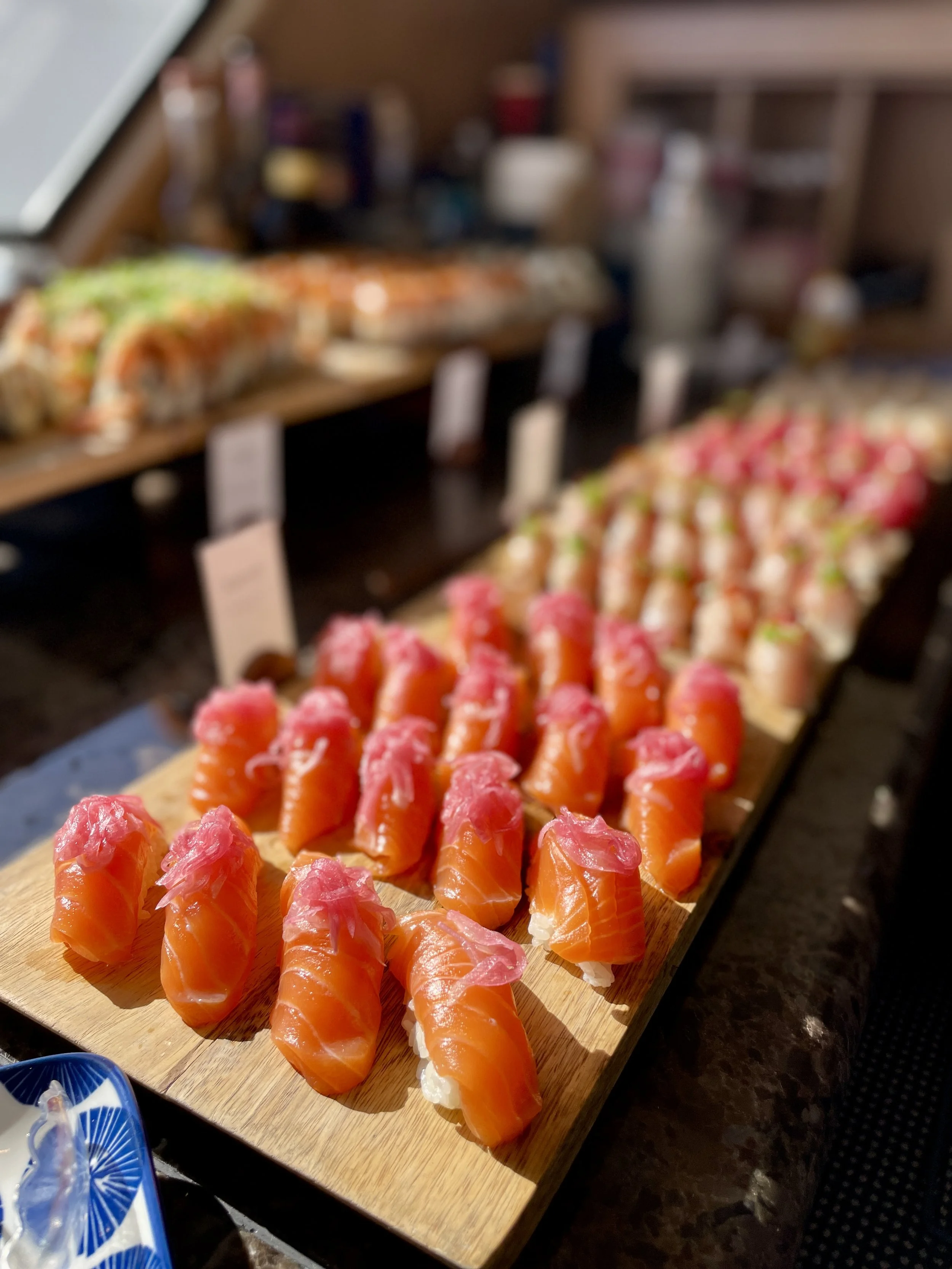 Close-up of assorted sushi rolls and nigiri on a wooden serving board with pickled onion on top