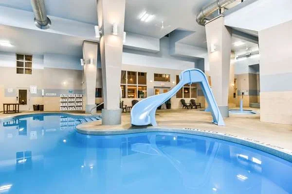 Indoor swimming pool with a small blue water slide and lounge chairs.