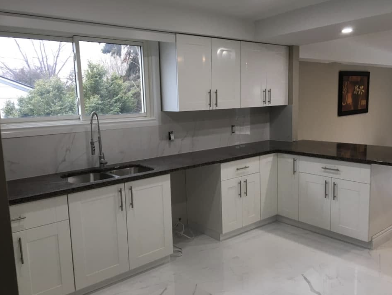 Modern kitchen with white cabinets, dark granite countertops, a sink under a window, and a framed picture on the wall.