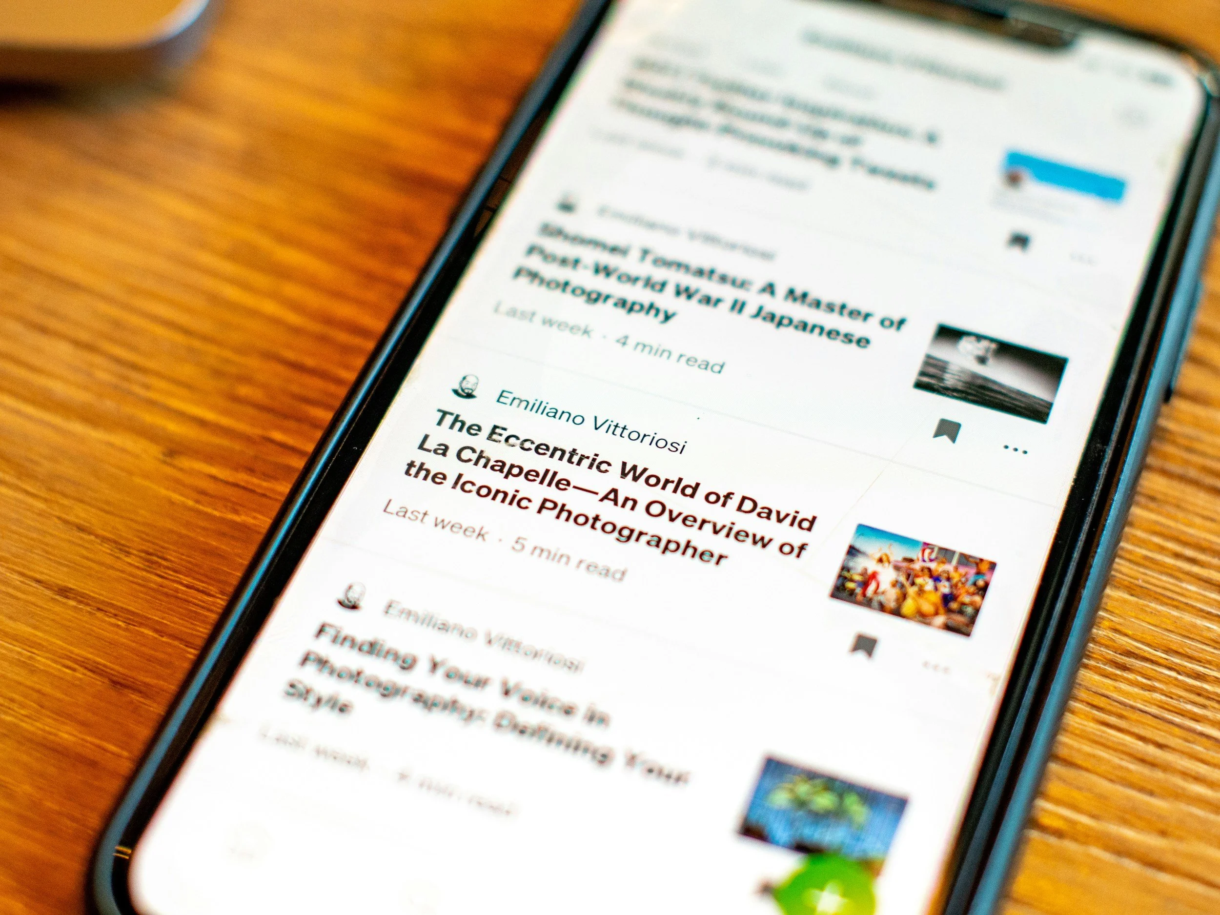 Close-up of a smartphone on a wooden surface displaying a list of articles or news stories, with some text and images visible.
