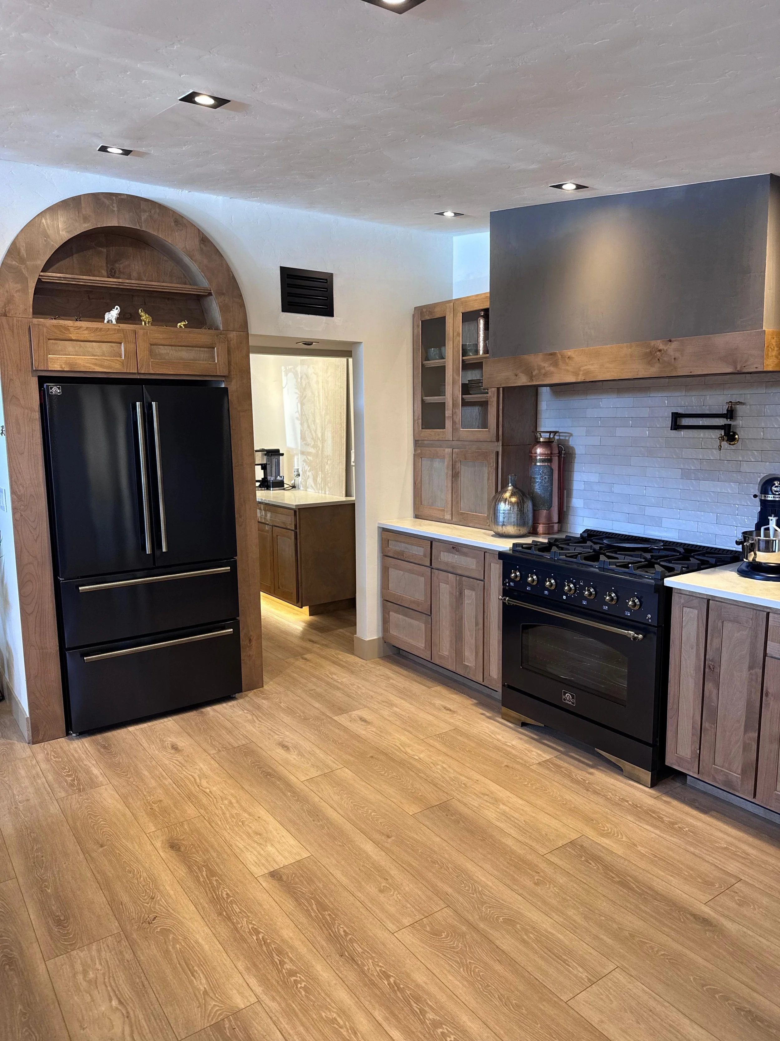 A modern kitchen with wooden cabinets, a black refrigerator, a black oven, and decorative items including vases and sculptures. The cabinets are above the counter and adjacent to a doorway leading to another room.
