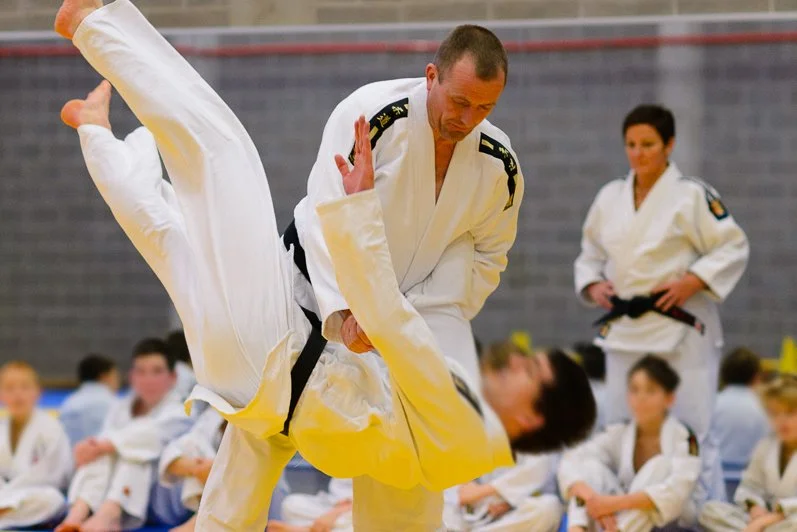 Martial arts students practicing judo in a dojo, with an instructor demonstrating a move while others observe.