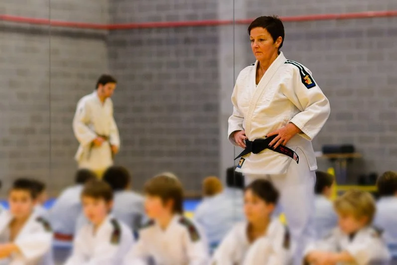 An adult woman judo instructor standing in front of children in judo uniforms during a class.