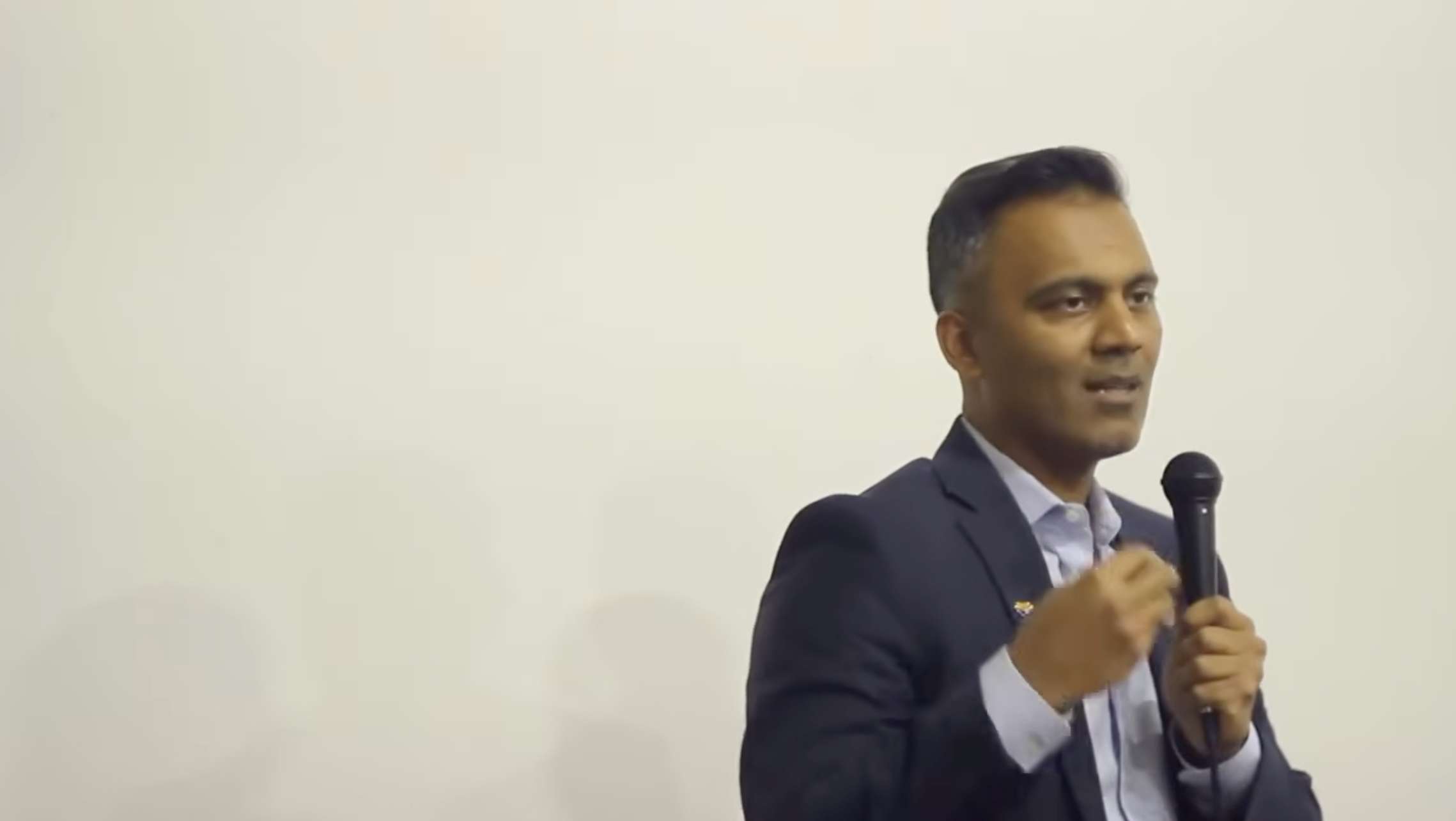 Man in suit speaking into a microphone during a presentation or speech.