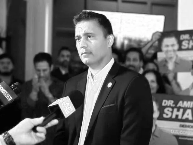 A man in a suit giving a statement to the press surrounded by supporters holding signs.