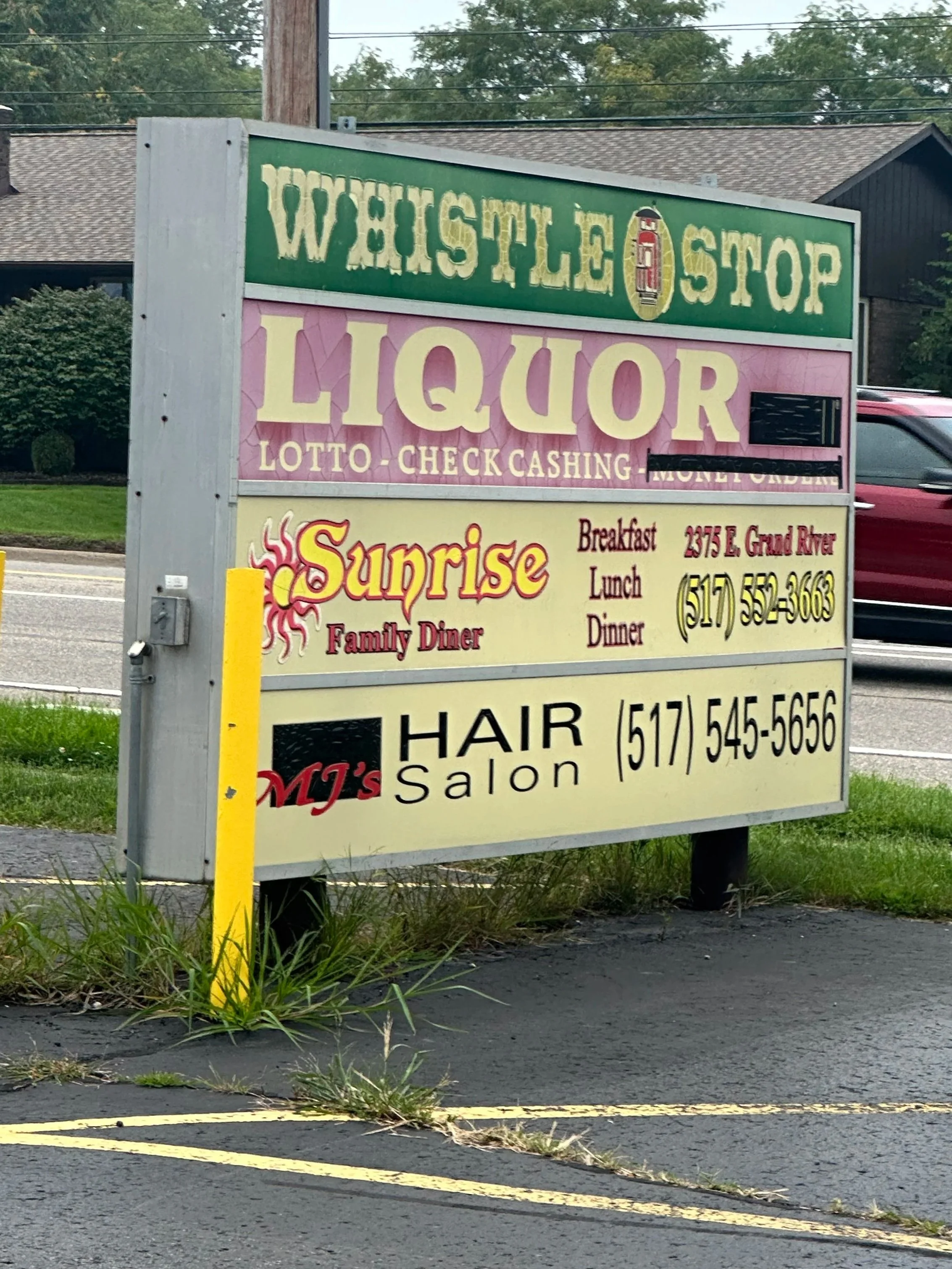 Sign advertising a wish list liquor store with additional offerings such as lotto, check cashing, and family dinner. The sign is located outside near a parking lot with some tire marks and patches of grass.