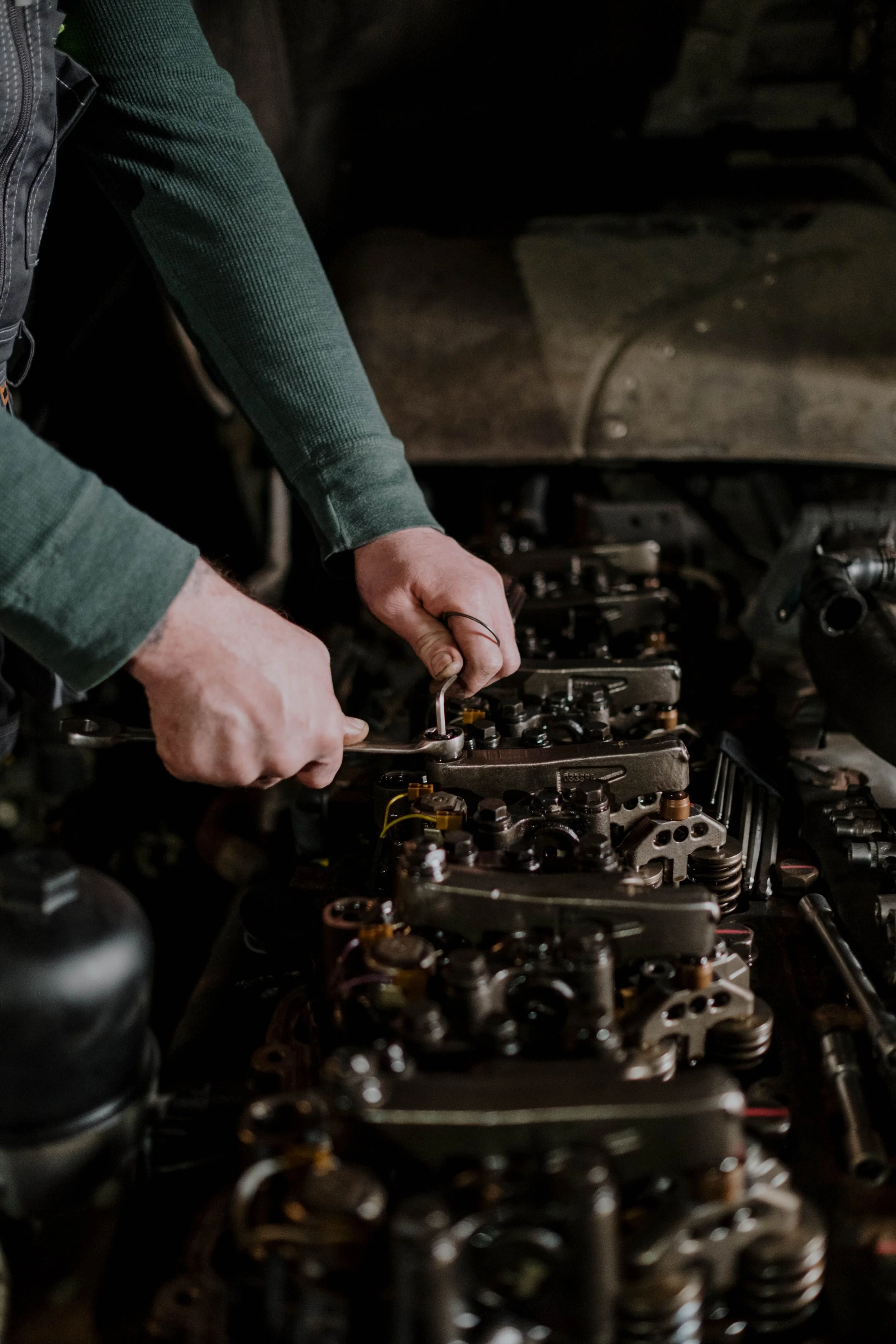 A person working on an engine, tightening or loosening bolts on valve components inside a mechanical engine.