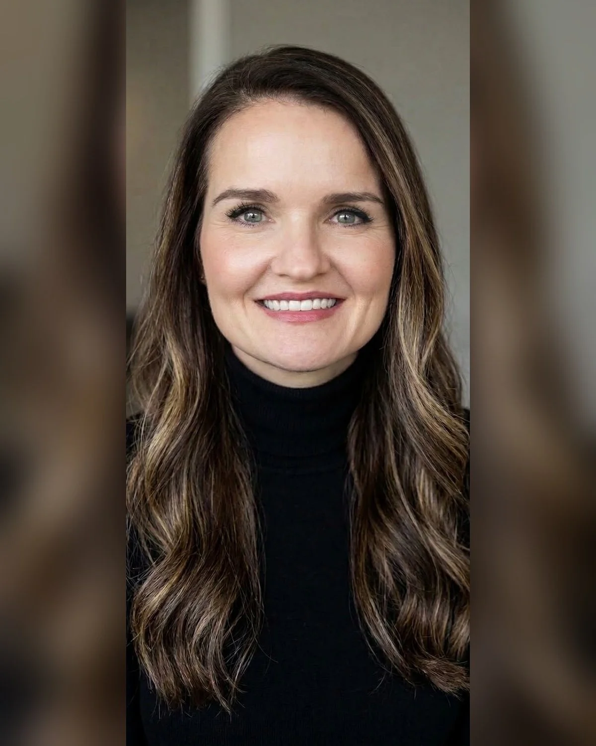 Portrait of a smiling woman with long wavy brown hair, wearing a black turtleneck sweater.