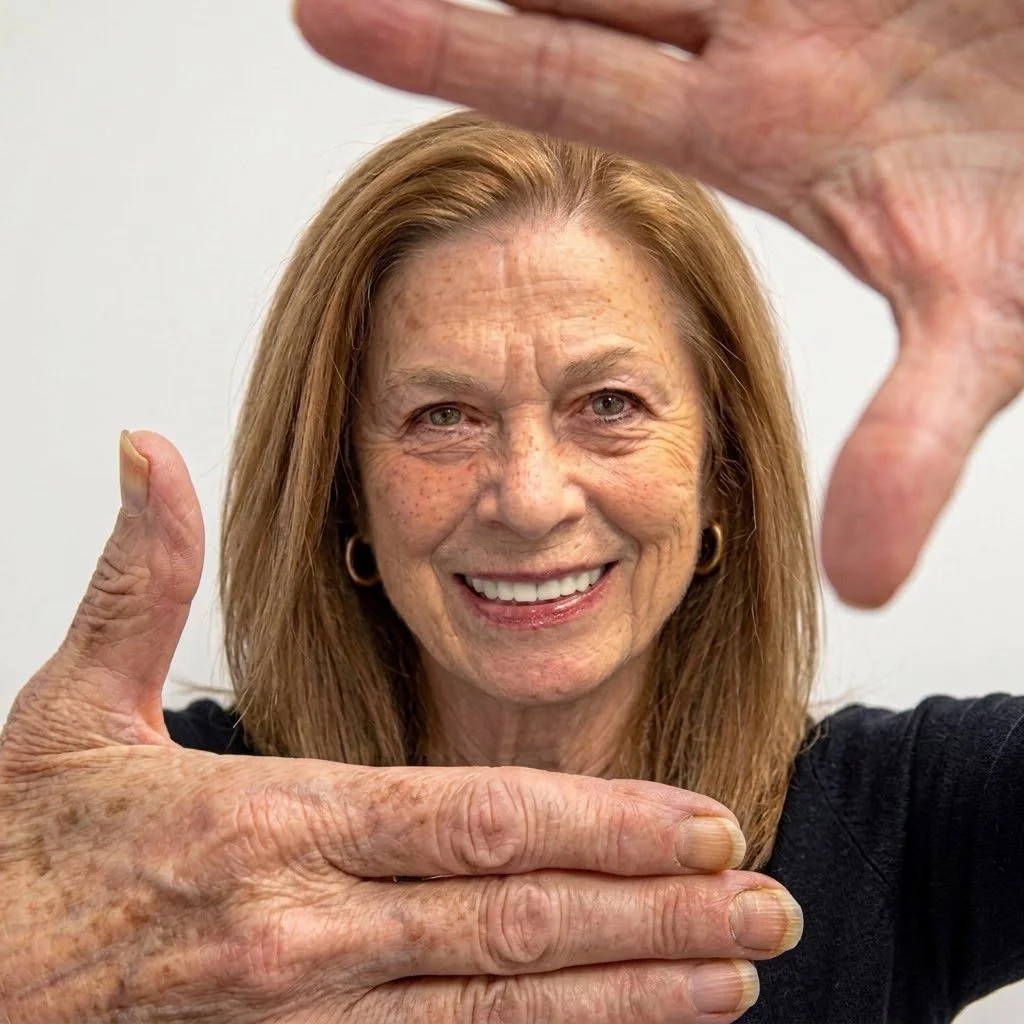 A smiling older woman with red hair making a frame with her hands around her face.