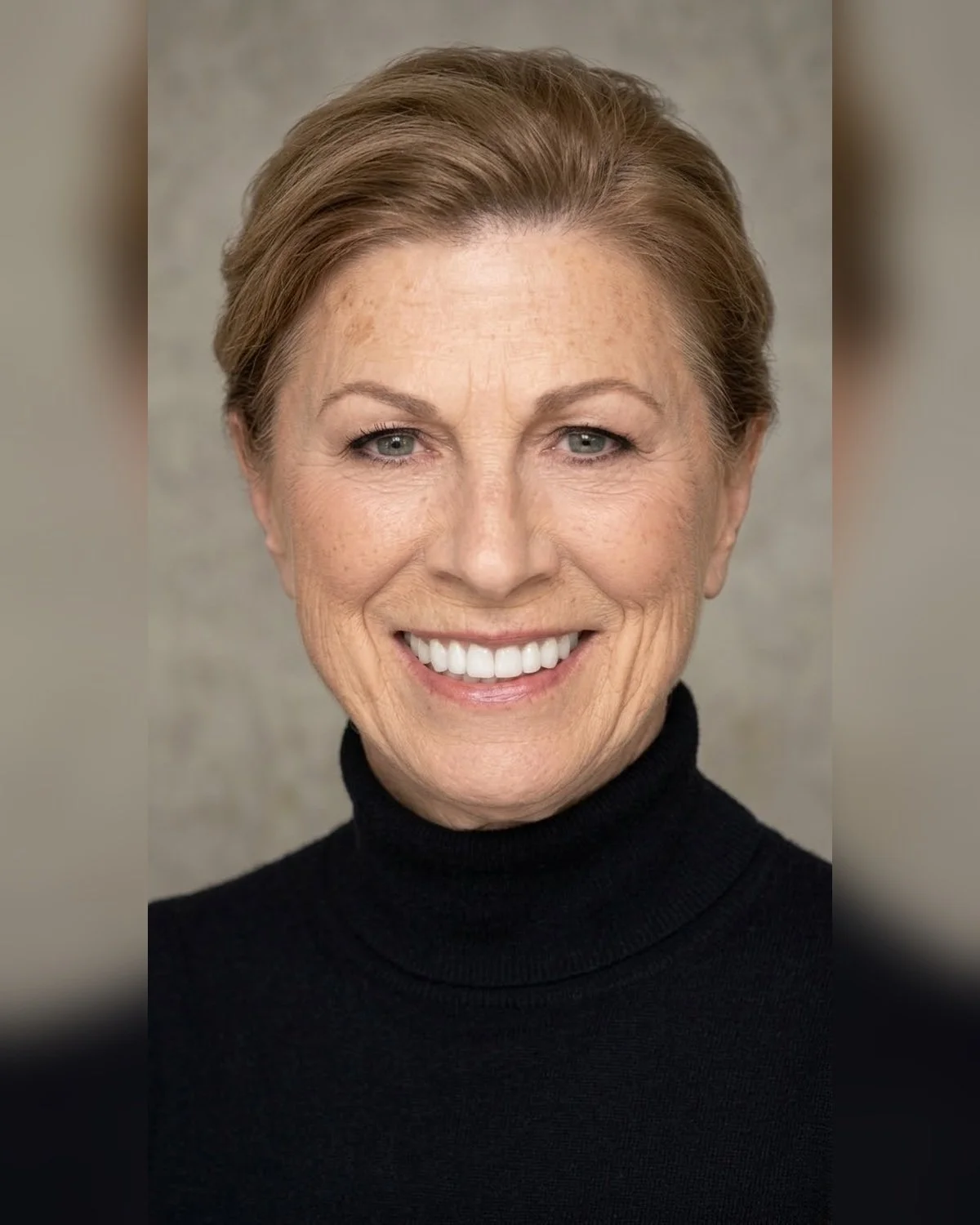 Close-up photo of smiling woman with short auburn hair, wearing a black turtleneck, against a neutral background.