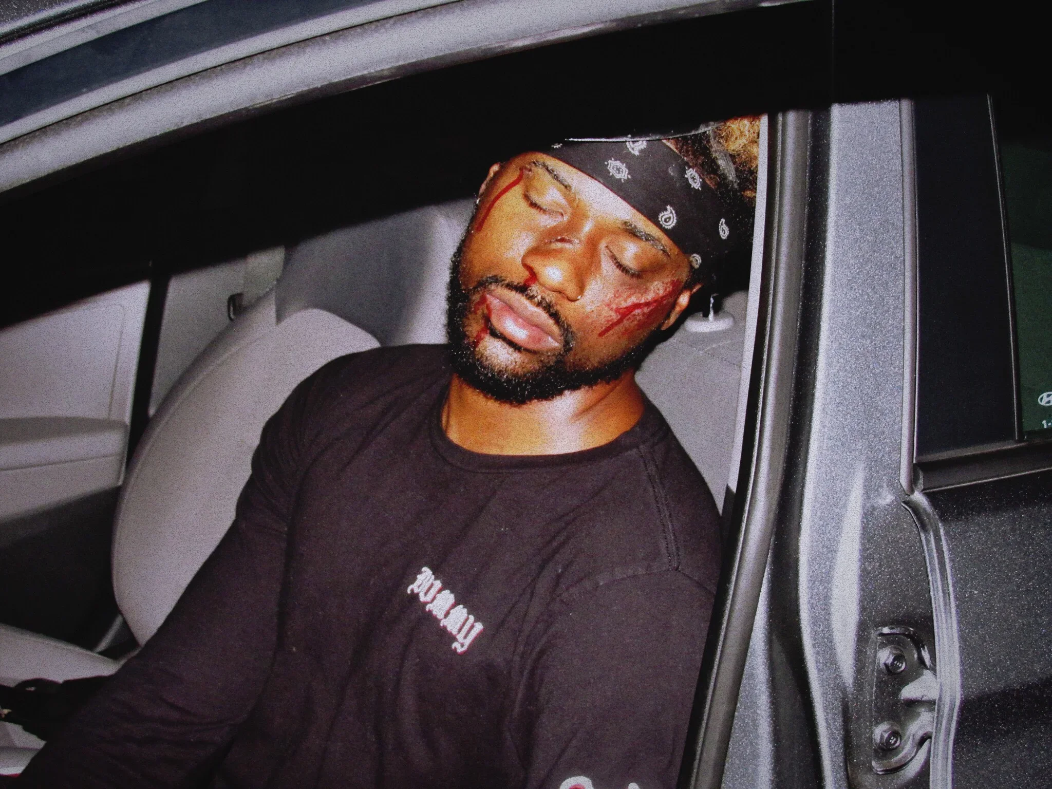 A man with a beard and a bandana on his head sleeping inside a washing machine or dryer, with the door open.