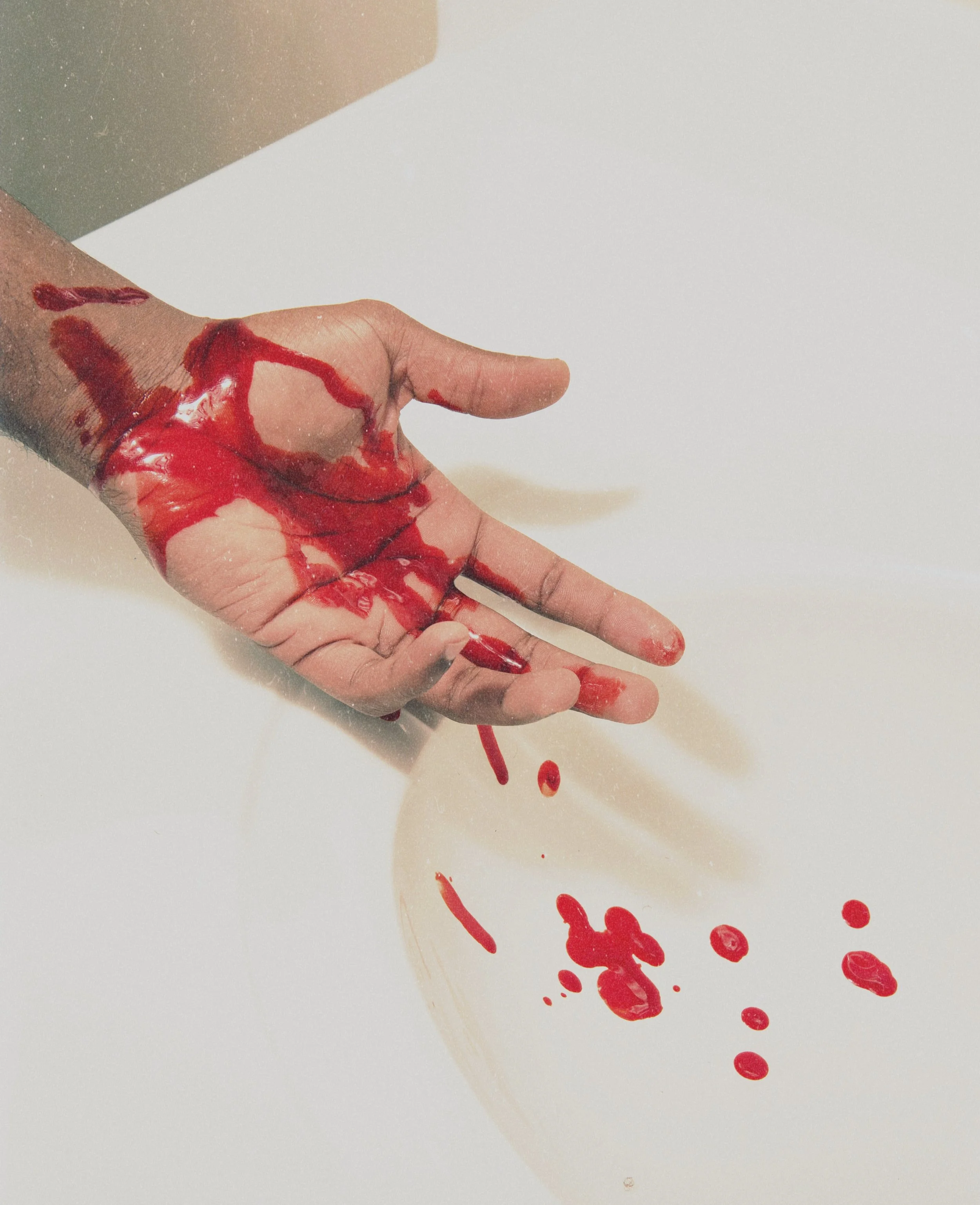 A hand with red paint or blood, palm facing up, spilling onto a white surface.