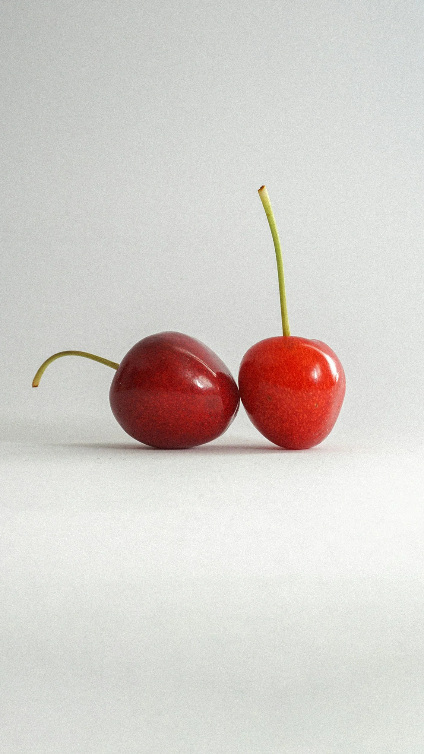 Two cherries, one on its side and one upright, on a plain white background.