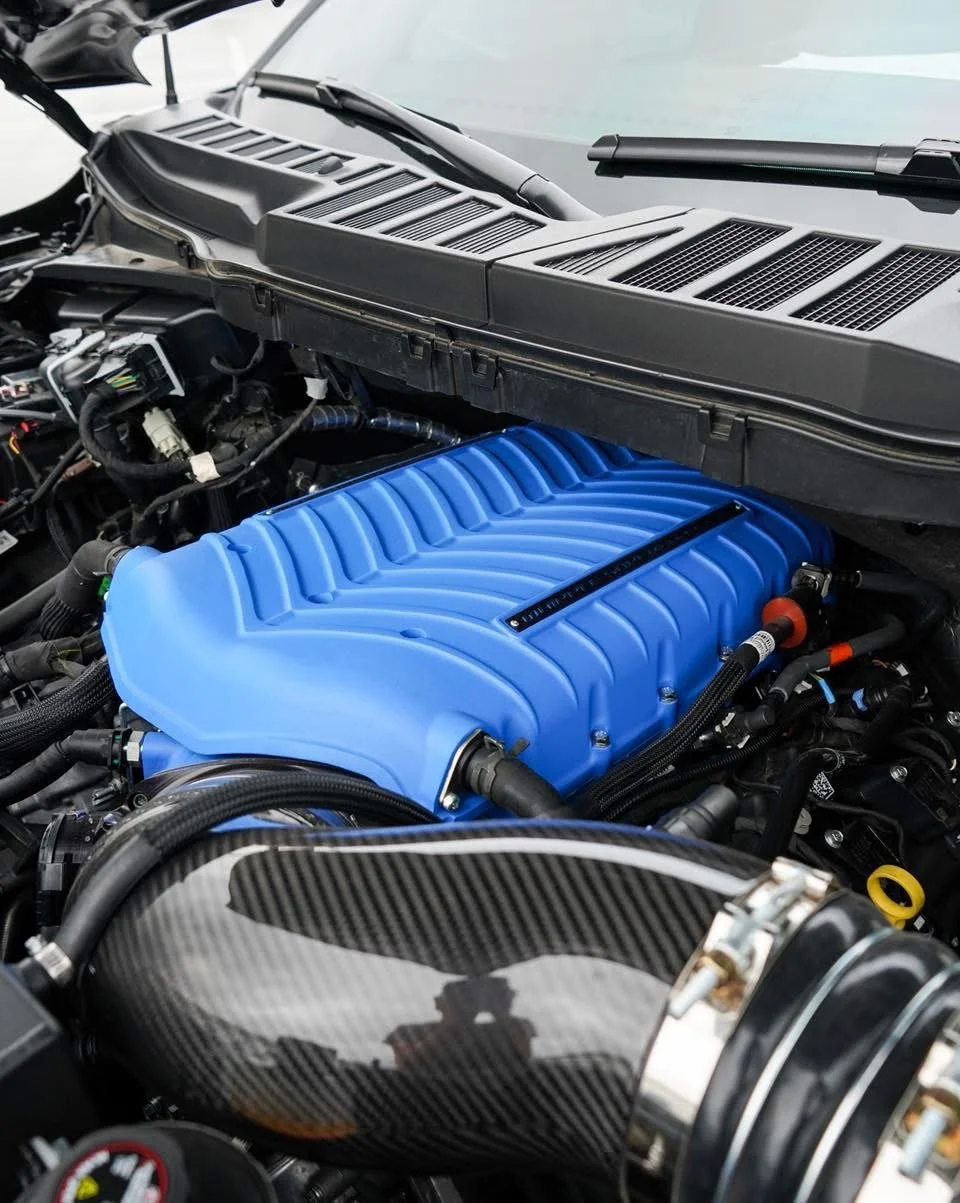 Close-up of a car engine with a prominent blue intake manifold and a carbon fiber air intake pipe.