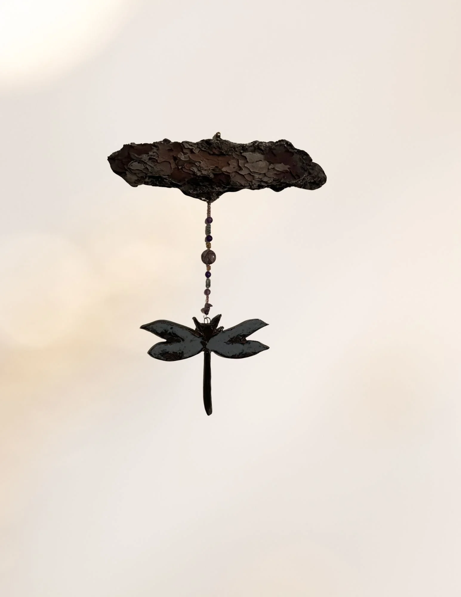 Hanging decorative wind chime with black metal flower and beaded chain against a light background.