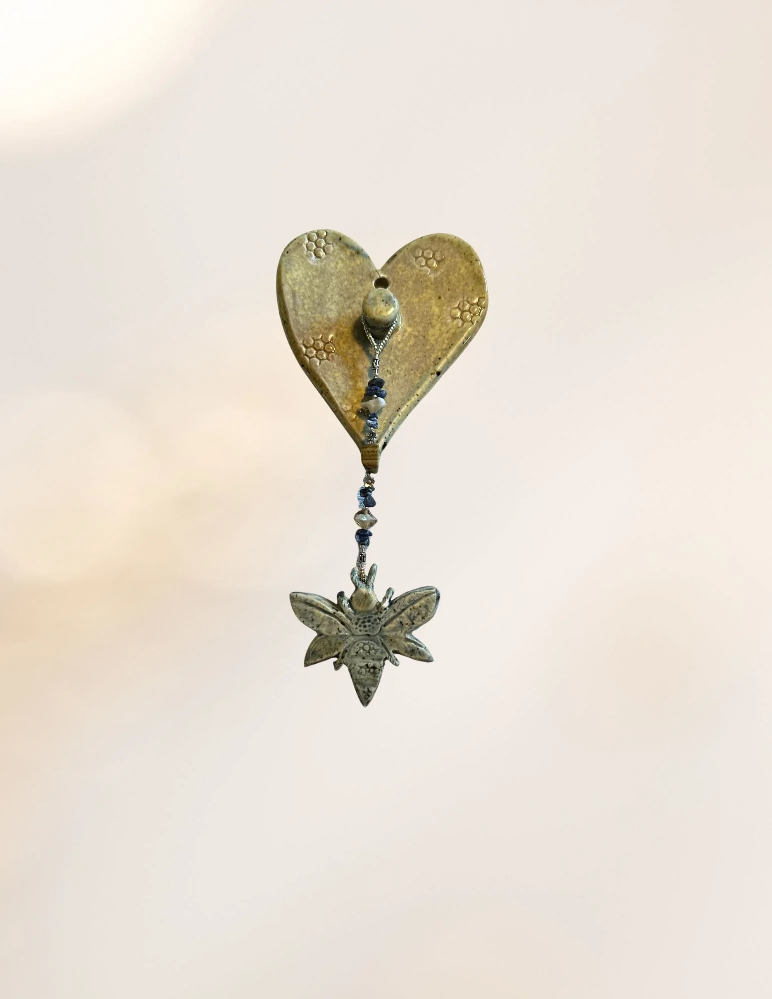 A decorative hanging ornament featuring a star-shaped, metallic heart with a small chain and fish-shaped charm beneath it, against a plain, light-colored background.