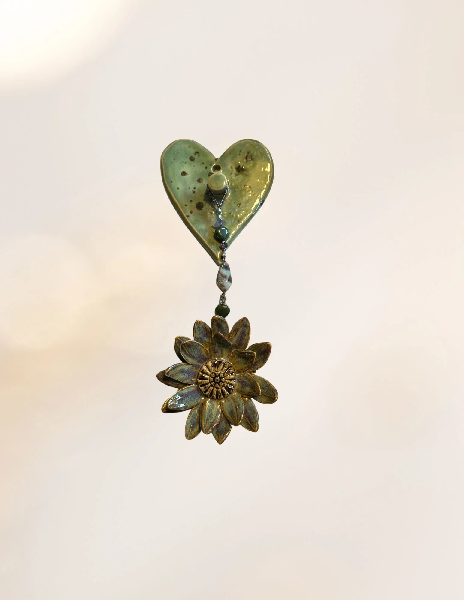 Decorative hanging object featuring a small green heart-shaped ornament with dark spots, a series of beads, and a metal flower pendant at the bottom.