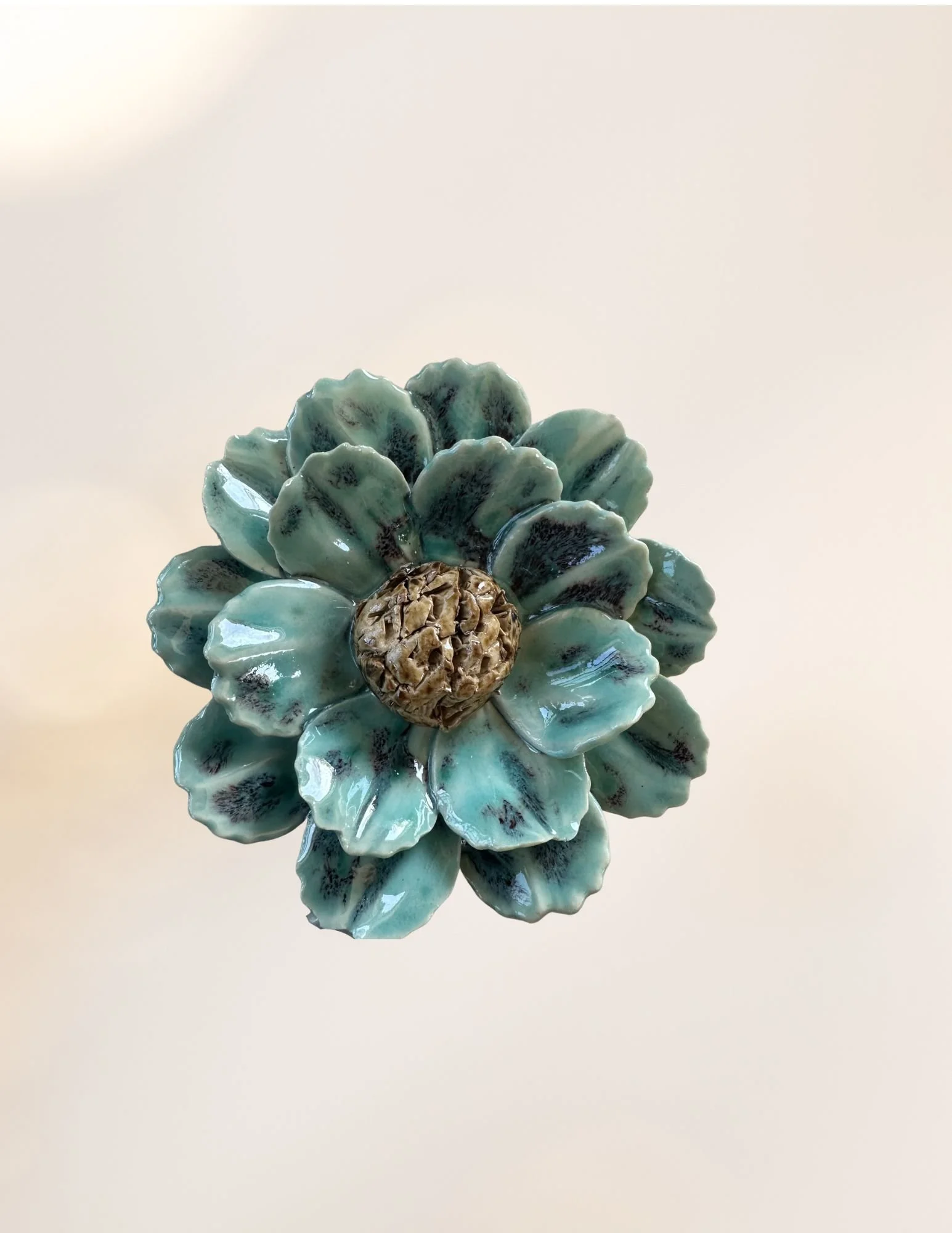 Ceramic flower sculpture with blue and green petals and a textured beige center, on a plain light background.