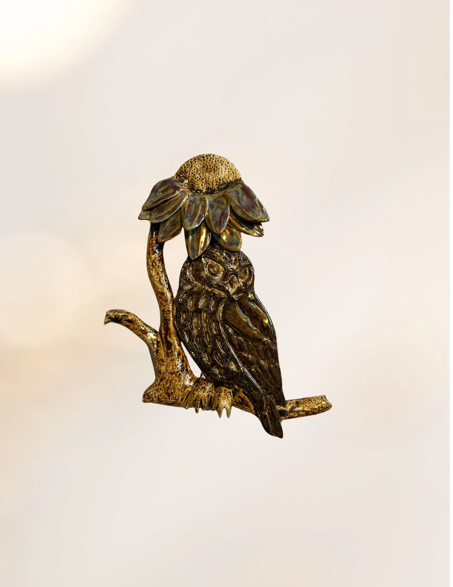 A decorative metal sculpture of an owl perched on a branch, with a sunflower-like design on its head.