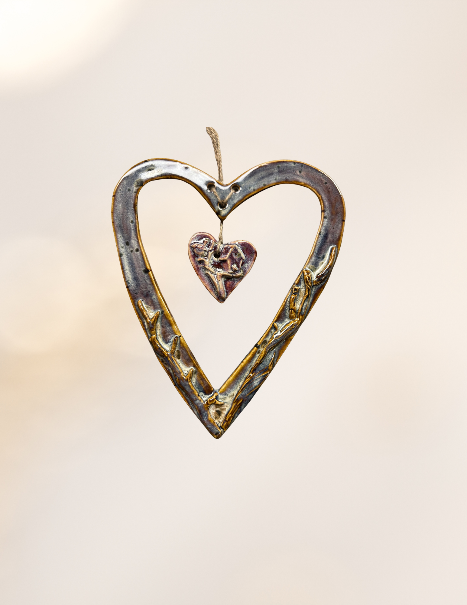 A metal heart-shaped ornament with smaller heart detail inside and a hanging string, set against a plain light background.