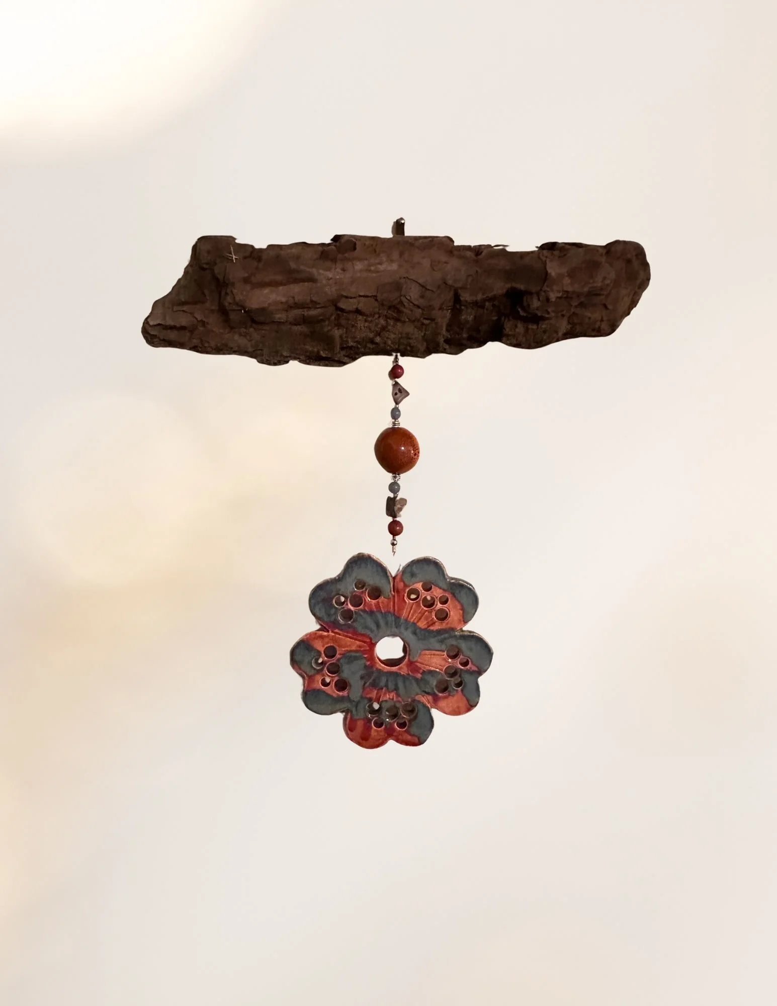 A hanging decoration featuring a butterfly-shaped ornament with holes, beads, and a wooden piece on top, set against a plain background.